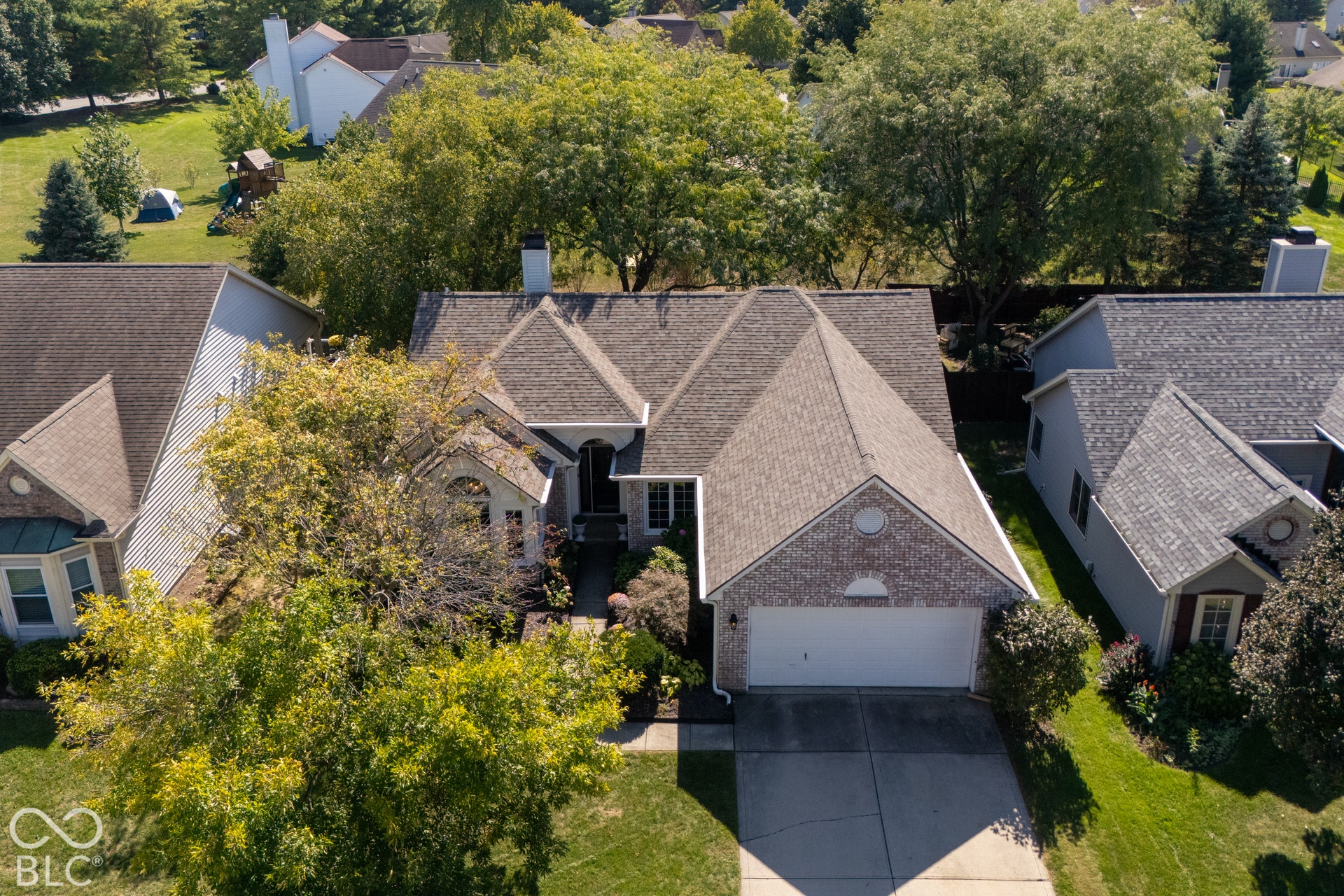 Brick facade residence featuring a multi-gabled roofline, attached two-car garage, arched entry, and mature landscaping