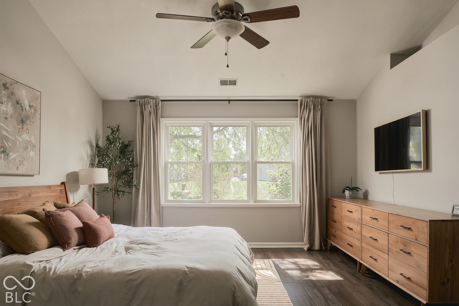 Vaulted ceiling with a ceiling fan, three pane window with drapes, and wood-finish flooring