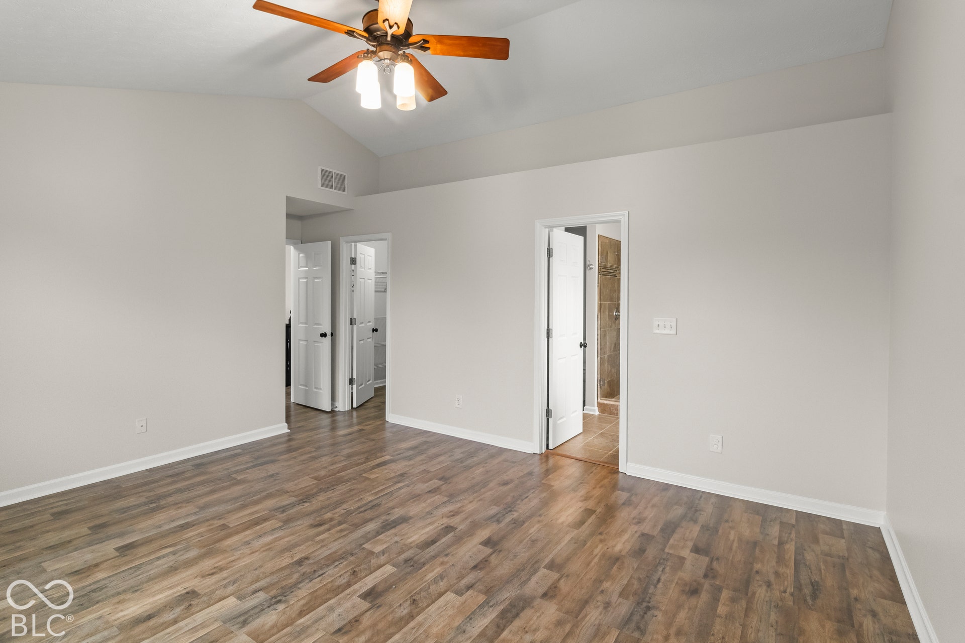 Vaulted ceiling with a wood-finish ceiling fan, wood-finish flooring, and white interior doors