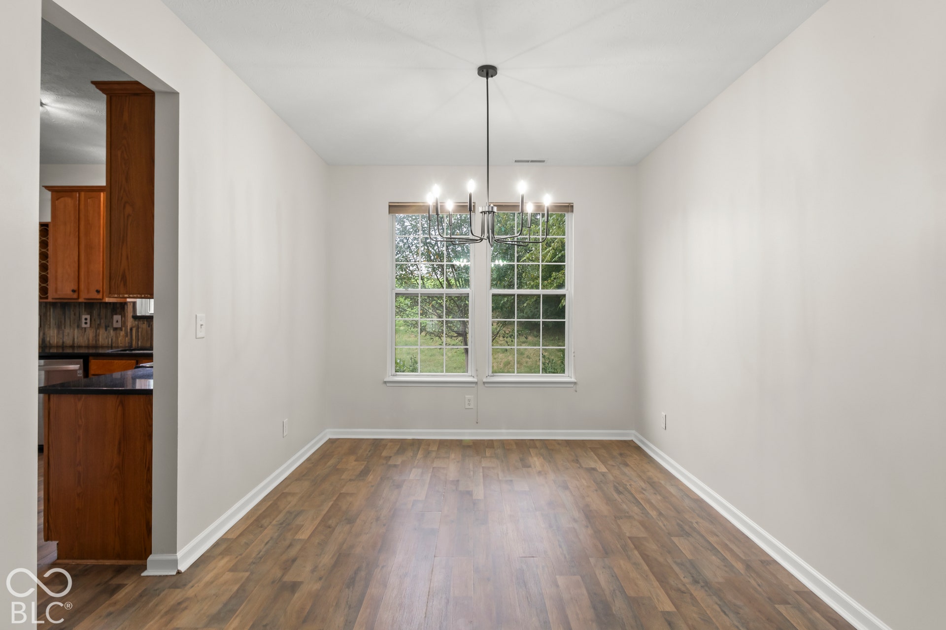 Wood-finish flooring, white trim, and a modern chandelier illuminate this bright space