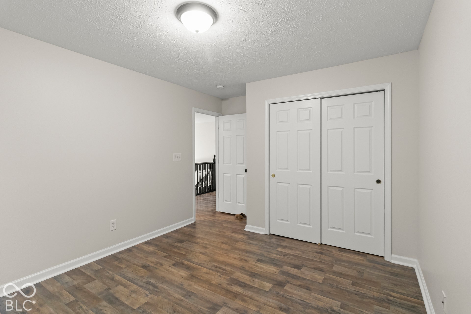 Wood-finish flooring, white paneled closet doors, neutral wall paint, overhead flush-mount lighting