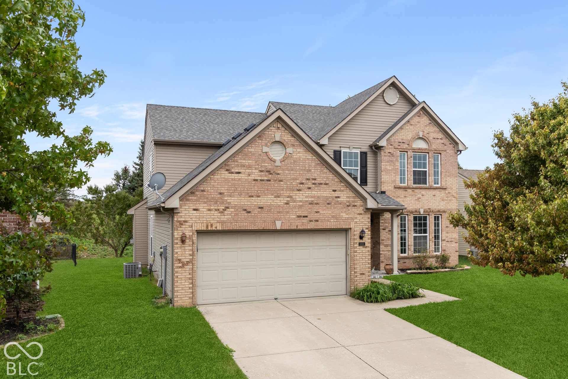 Brick facade with siding accents, attached two-car garage, concrete driveway, and front lawn