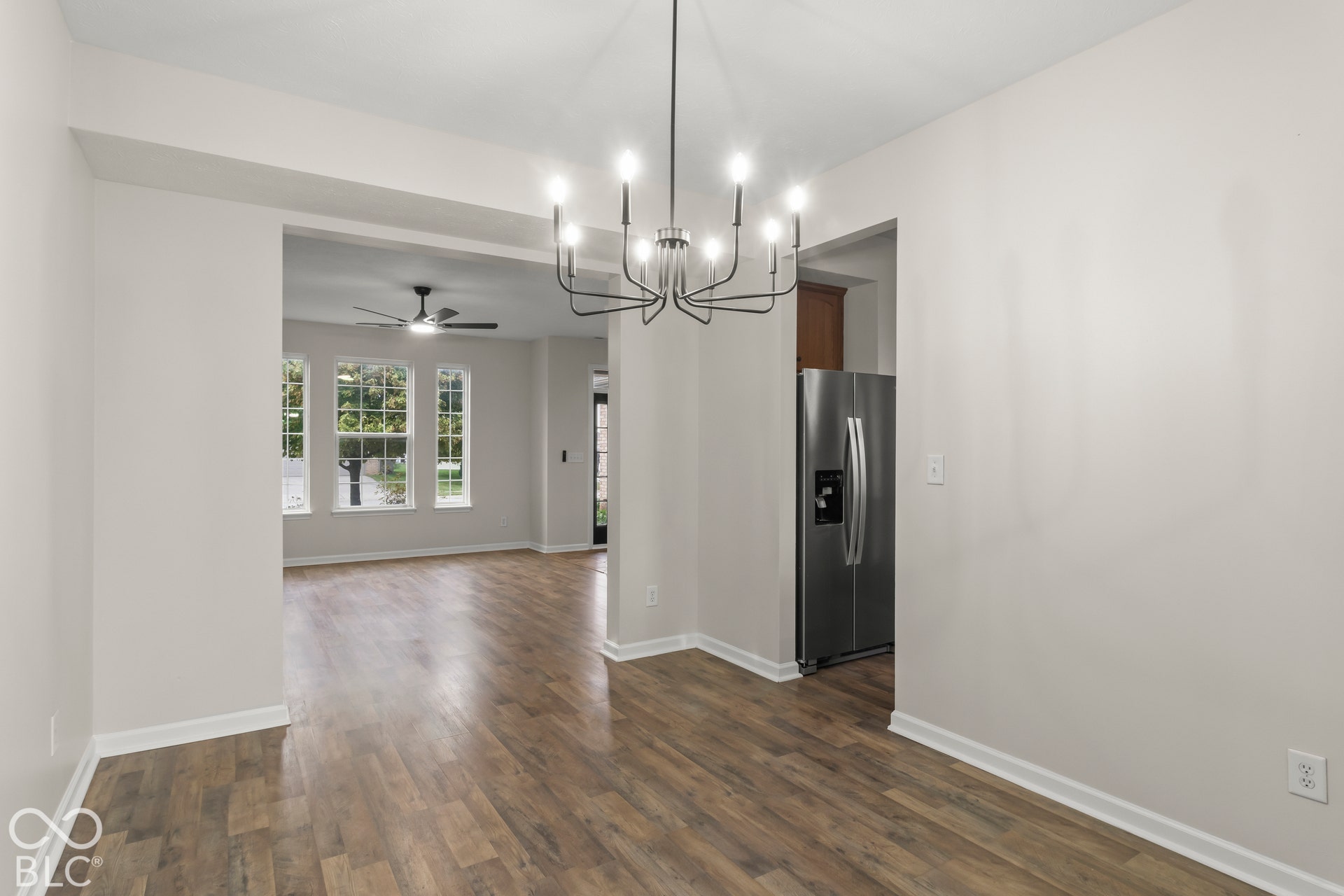 Wood-finish flooring throughout, modern chandelier, stainless steel refrigerator, and multiple windows providing natural light