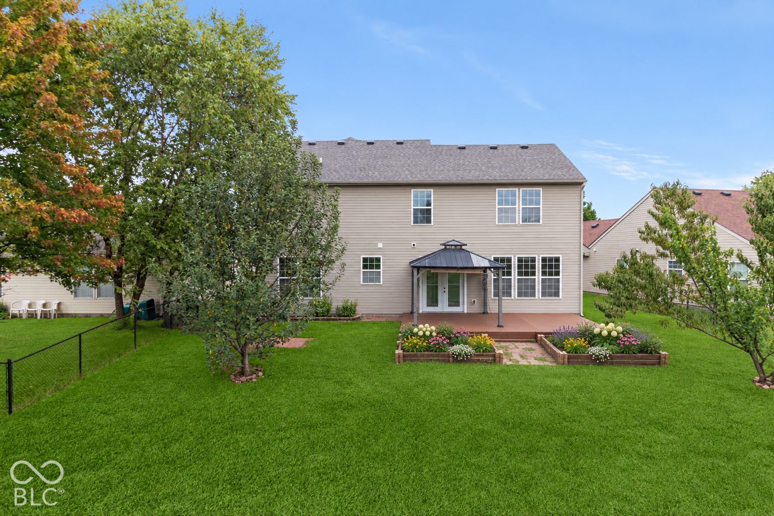 Expansive green lawn, multi-level deck, gazebo, and raised garden beds with established plantings