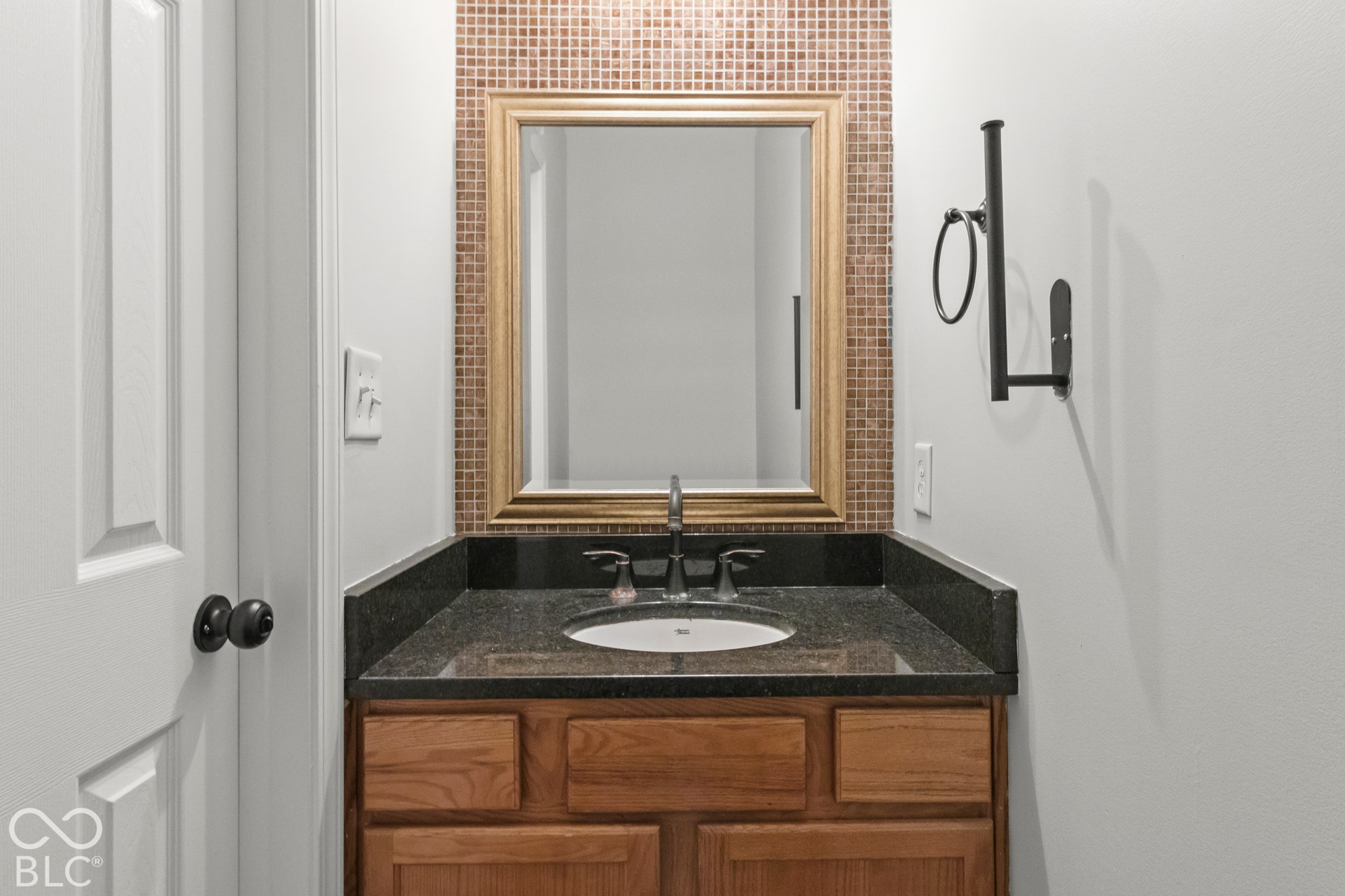 Wood-finish vanity with an undermount sink, dark stone countertop, and mosaic tile backsplash