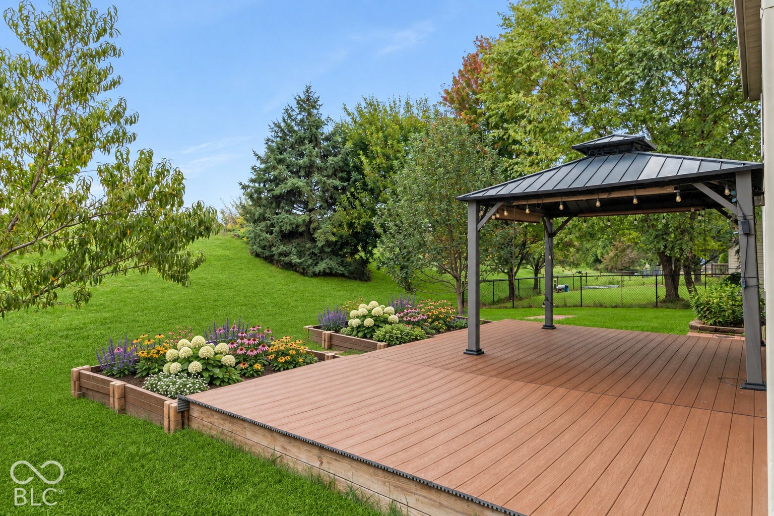 Expansive outdoor living area featuring a spacious composite deck, a metal-roofed gazebo, and built-in garden beds with various plantings