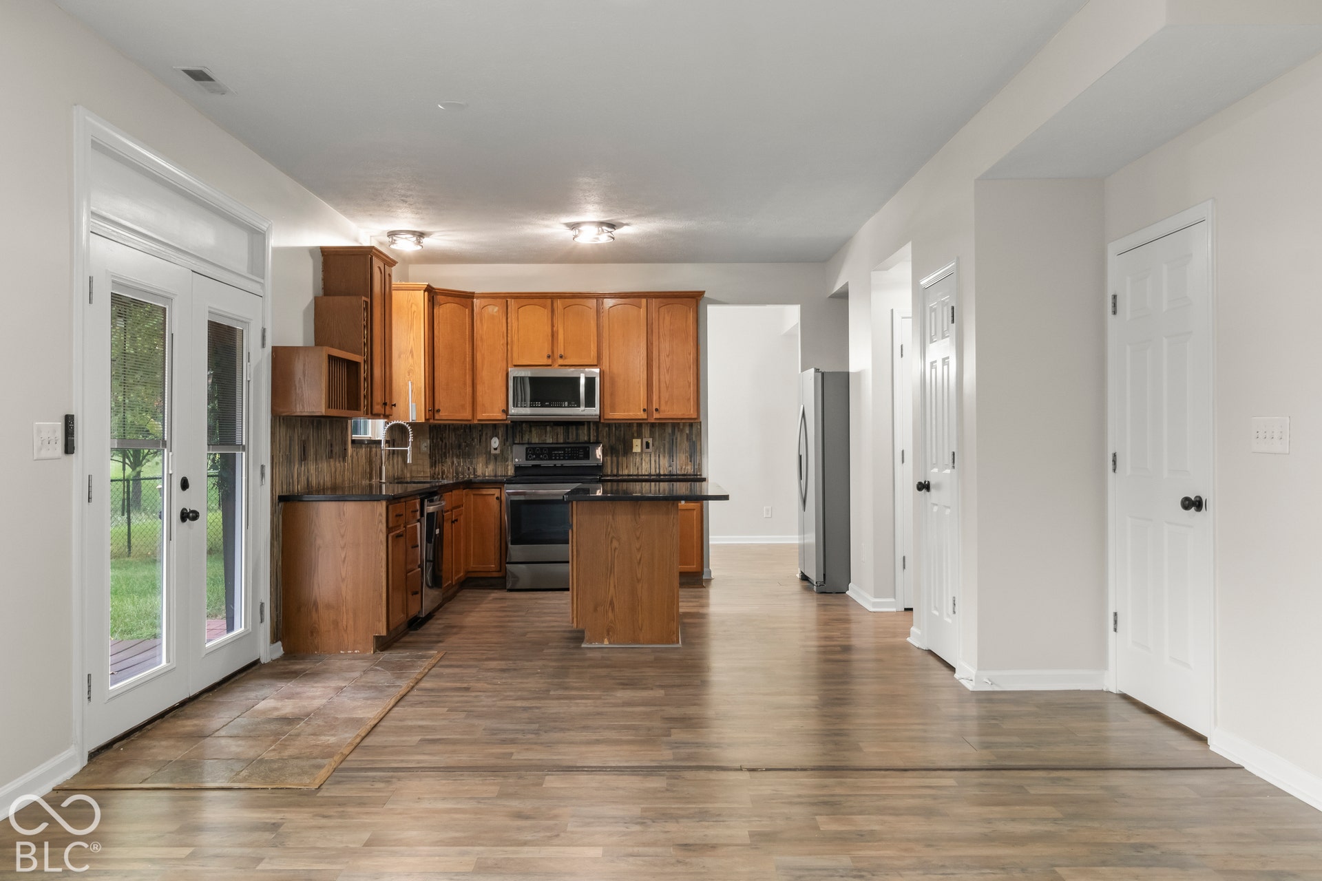 Wood-finish flooring throughout, wood cabinetry, built-in stainless steel microwave, black electric range, and french doors