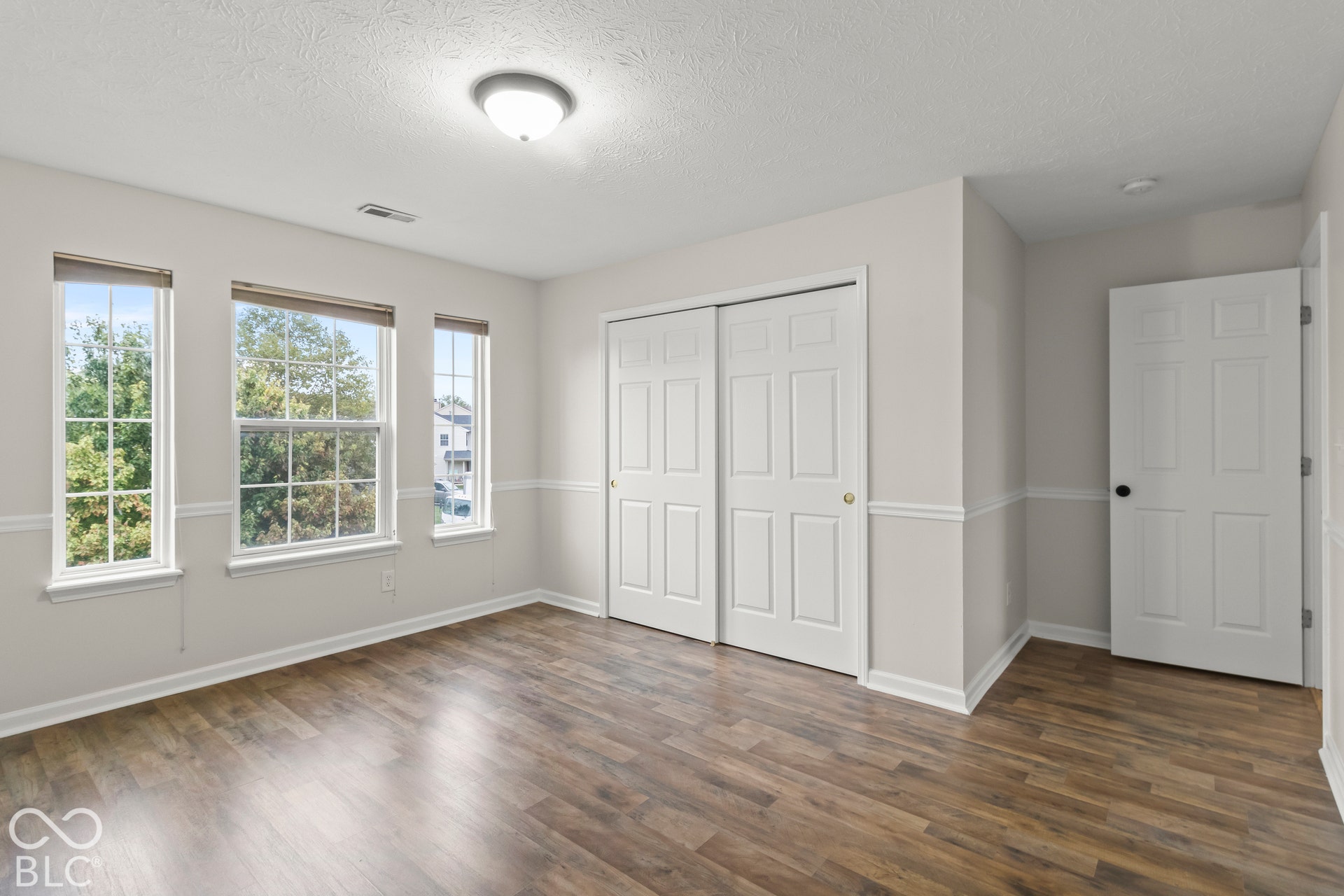 Wood-finish flooring, multiple windows, overhead lighting, bifold closet doors, and a paneled interior door