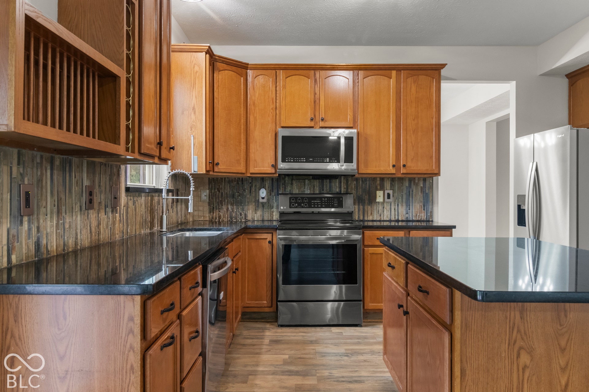 Kitchen featuring wood cabinetry, stainless steel appliances, dark countertops, and wood-look flooring
