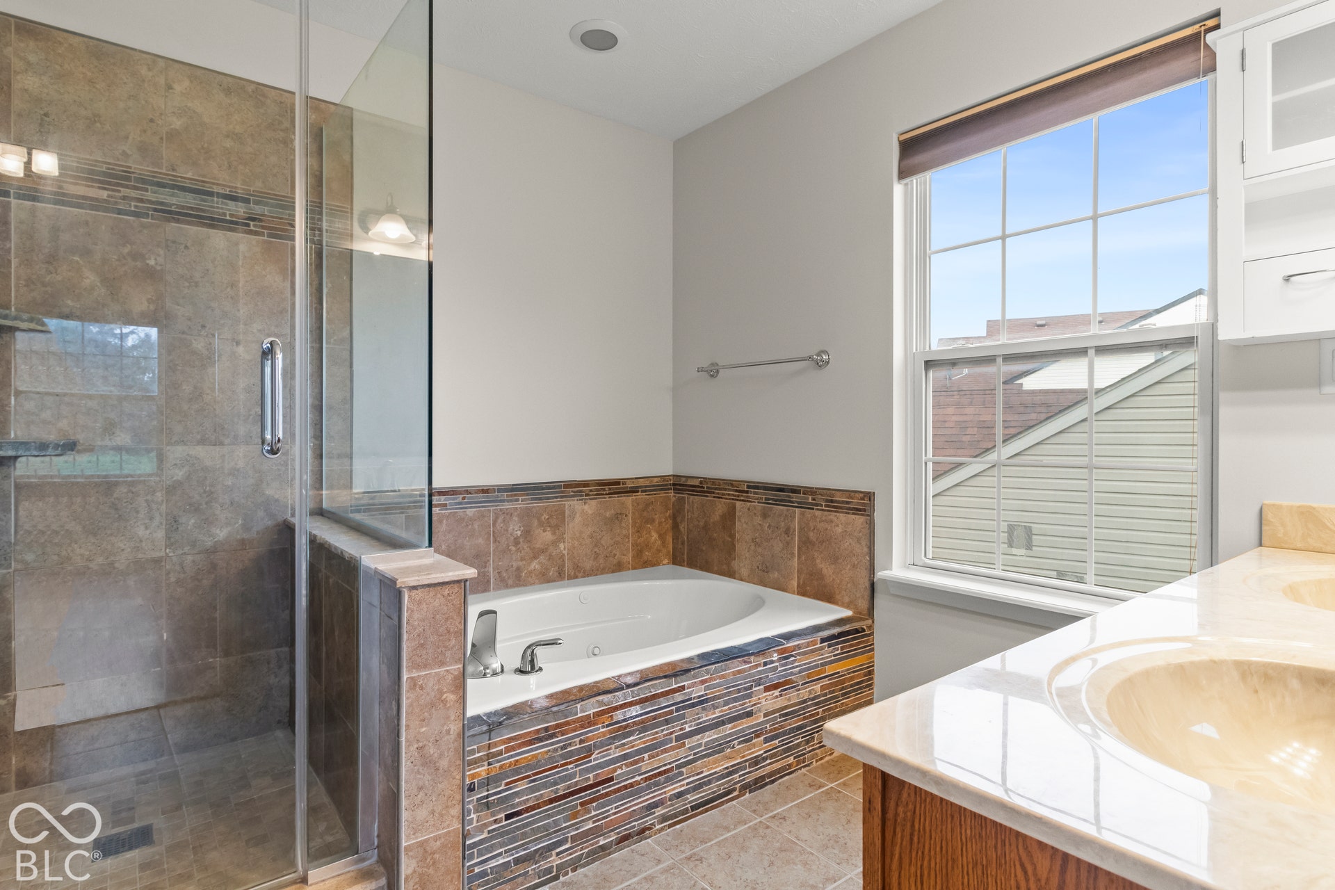 Glass-enclosed shower, jetted soaking tub with mosaic tile surround, dual vanity sinks, and built-in cabinetry