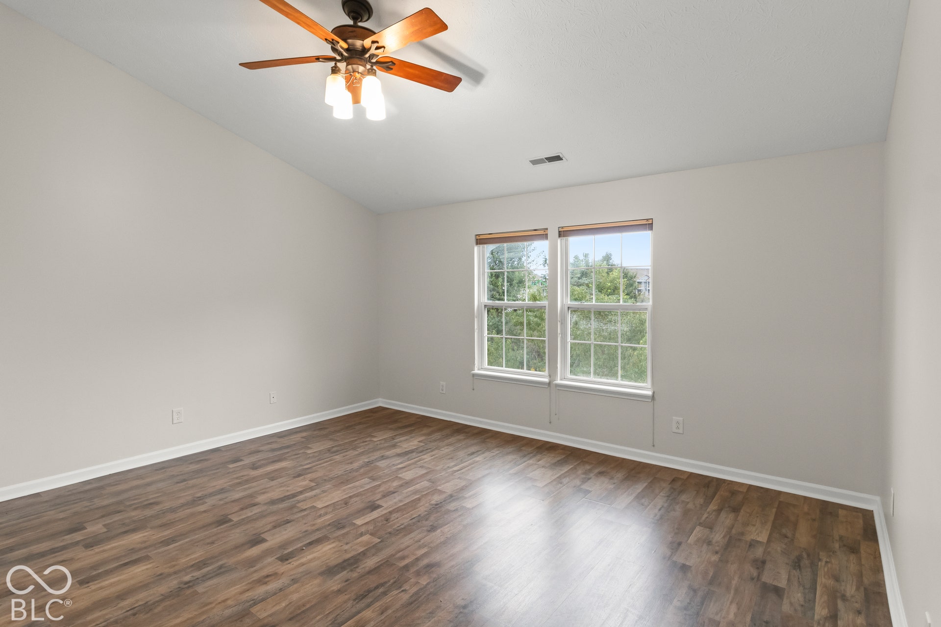 Wood-finish flooring, two large windows, vaulted ceiling, and a ceiling fan with light fixture