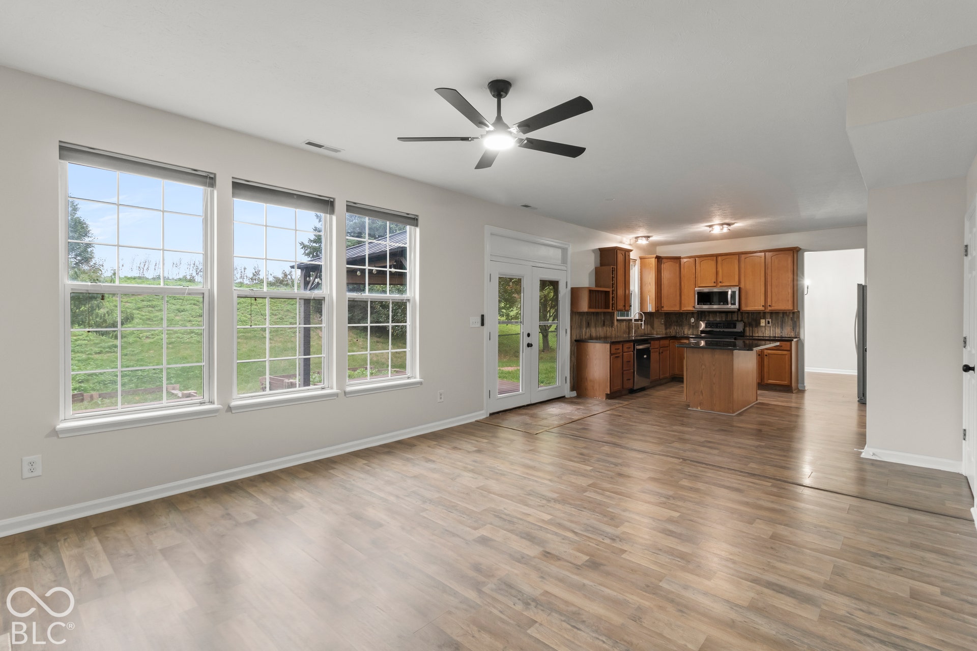 Wood-finish flooring, multiple windows with grid patterns, ceiling fan, double French doors, and a kitchen featuring wood cabinetry and an island