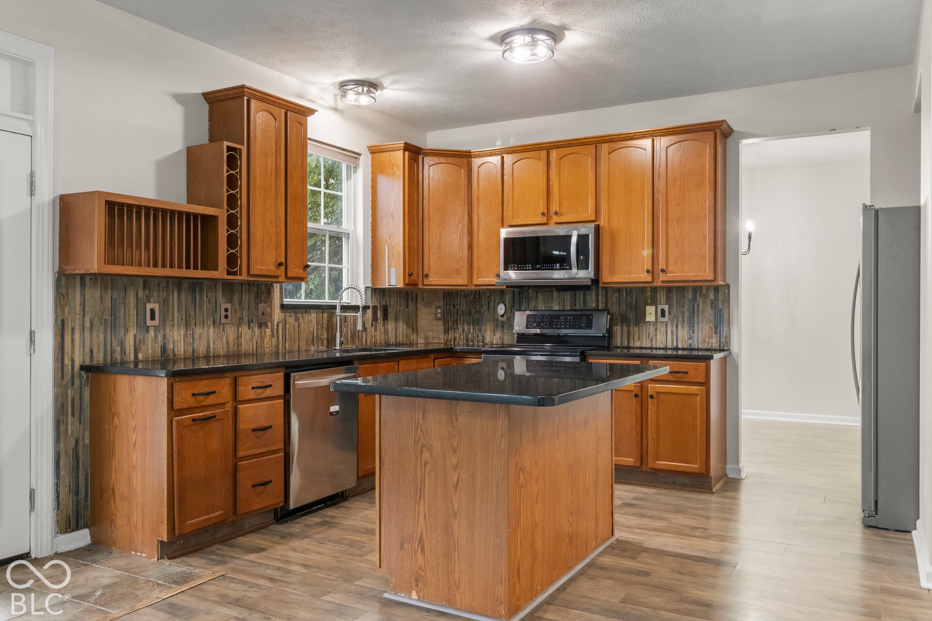 Kitchen featuring wood-finish cabinetry, built-in wine storage, a central island, dark countertops, and stainless steel appliances