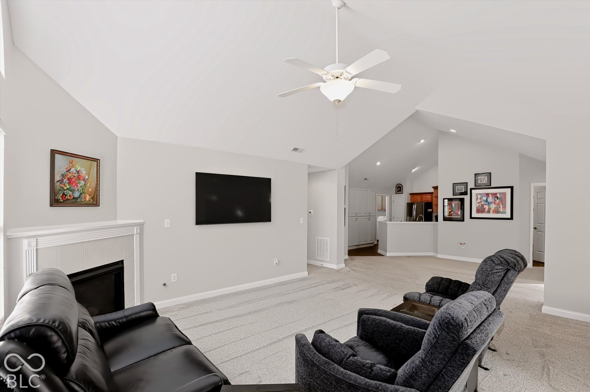 Vaulted ceilings with a ceiling fan, a fireplace with a mantel, and light-toned carpeting
