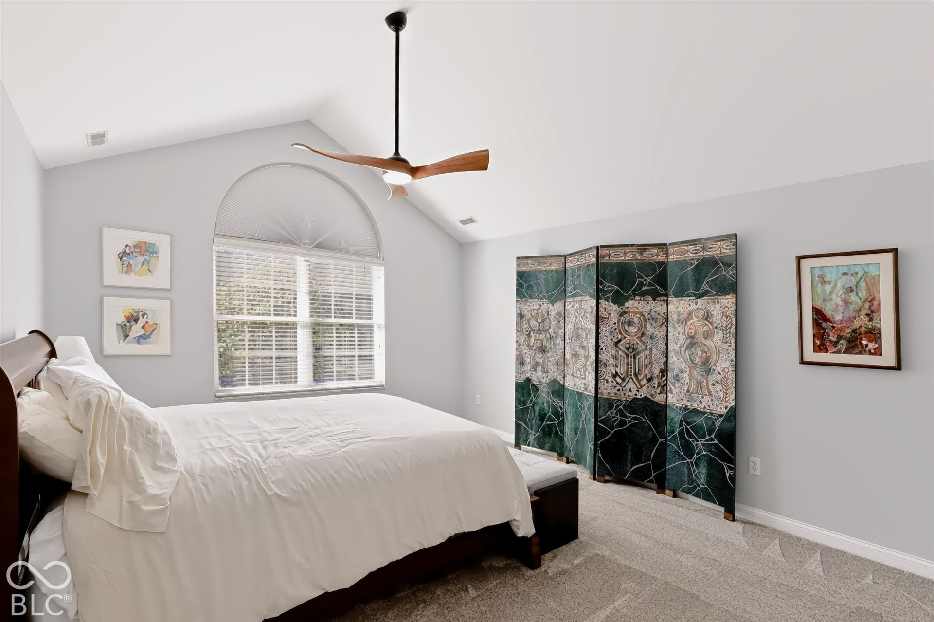 Vaulted ceiling with a wood-blade ceiling fan, arched window with horizontal blinds, and neutral-tone carpeting