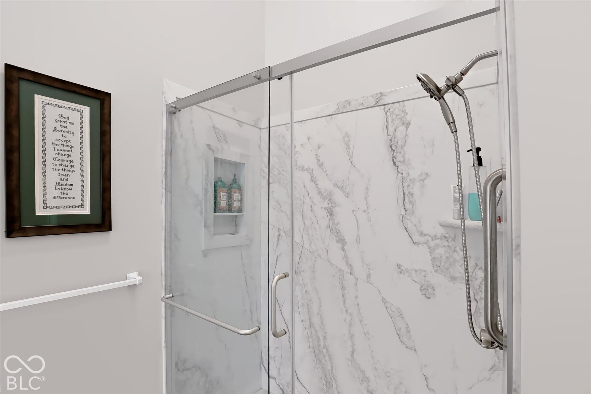 Shower enclosure with clear glass panel, marble-look wall surround, recessed shower niche, and brushed nickel shower fixtures