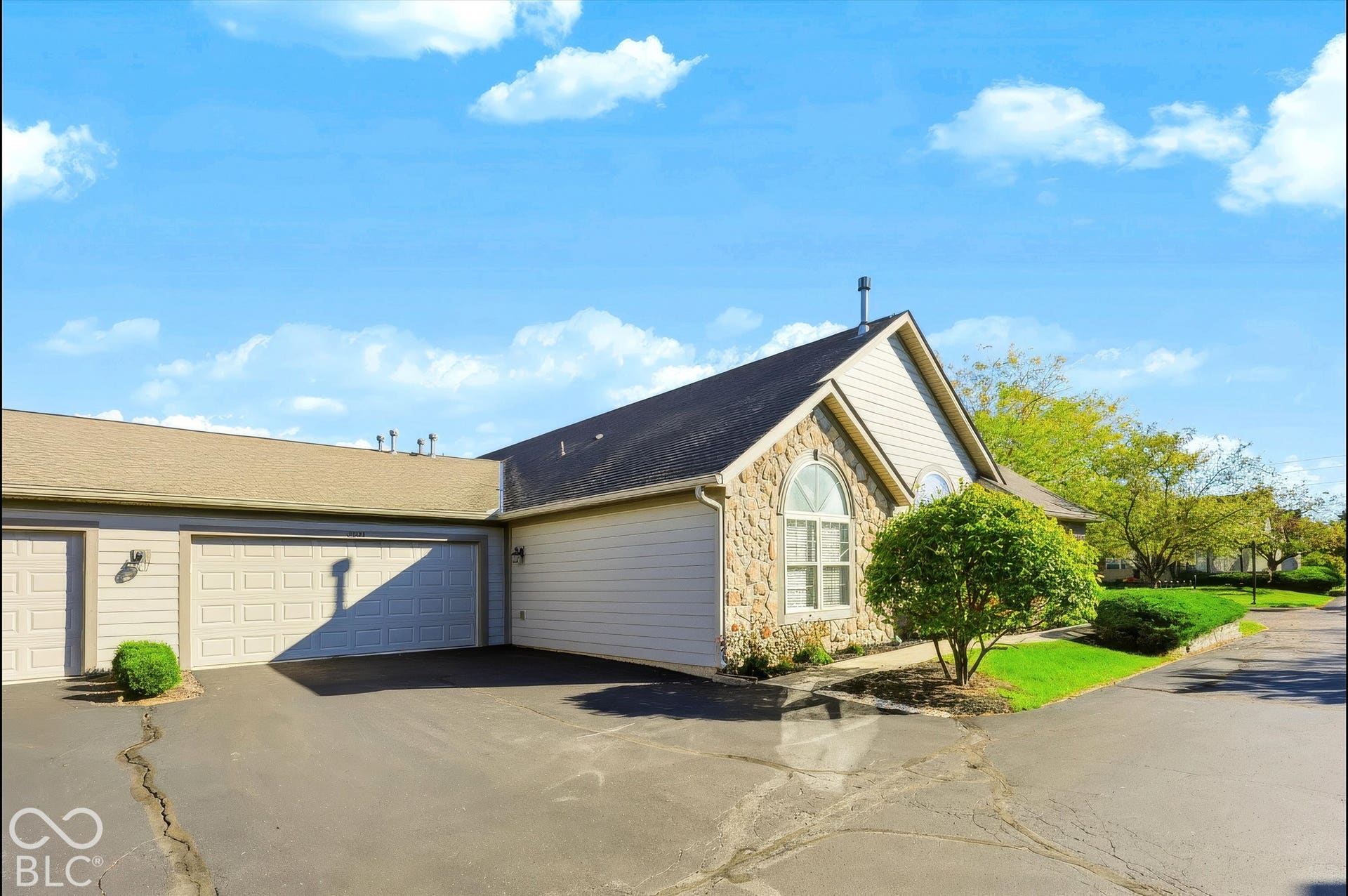 Exterior featuring stone veneer and siding facade, arched window with grilles, attached two-car garage, and established landscaping