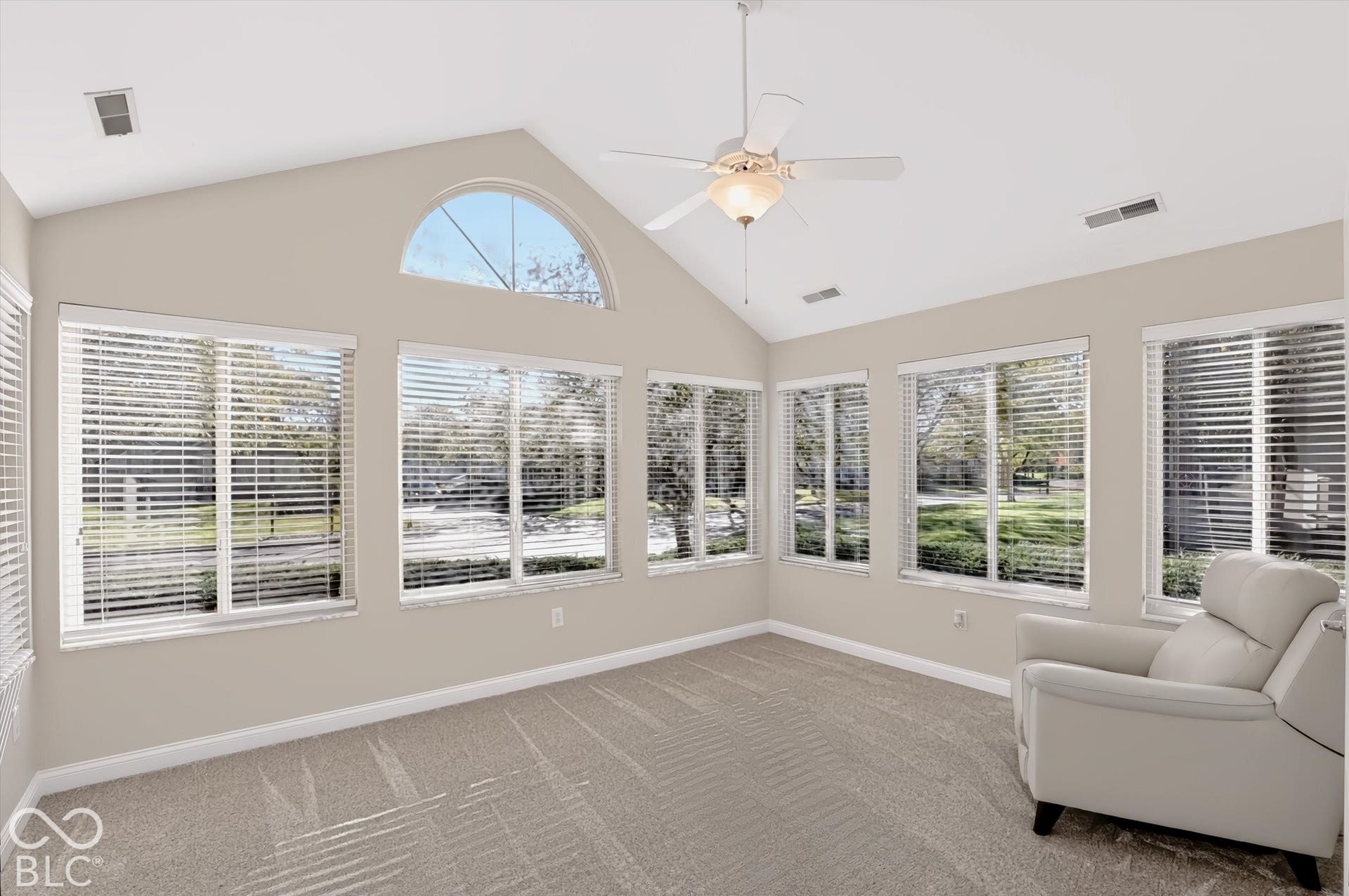 Vaulted ceiling with an arched window, multiple windows, ceiling fan, and neutral carpet flooring
