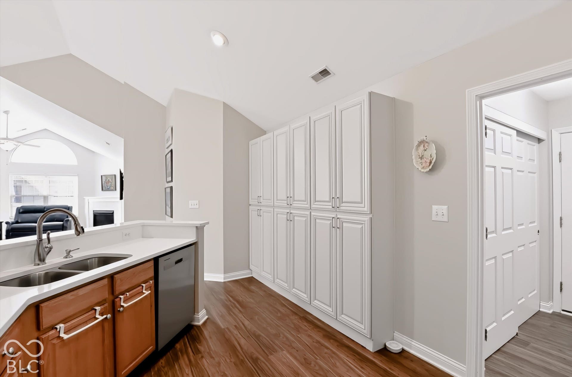 Kitchen featuring wood-finish flooring, white cabinetry, a double basin sink with a gooseneck faucet, light-toned countertops, and a built-in dishwasher