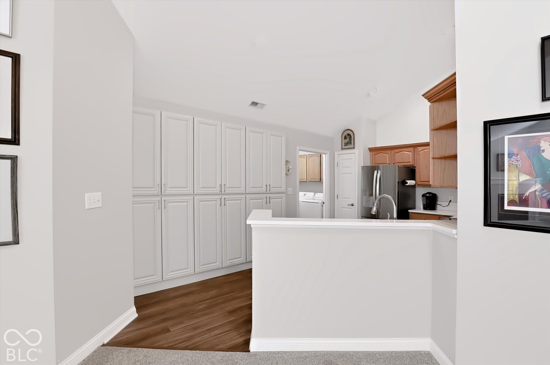 Integrated kitchen with wood-finish flooring, white cabinetry, and stainless steel appliances
