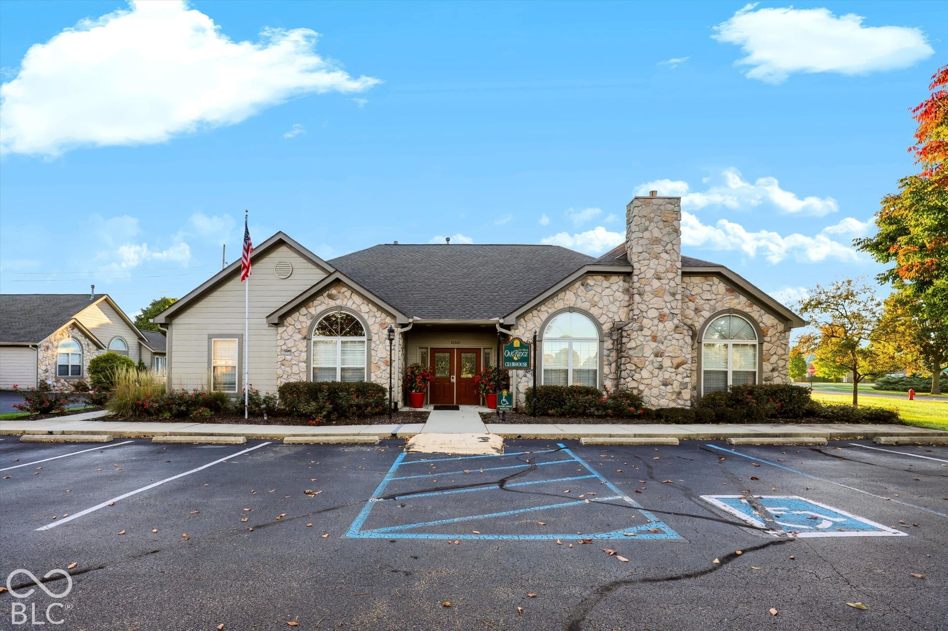 Stone facade with arched windows, light-toned siding, a prominent stone chimney, and a paved parking area