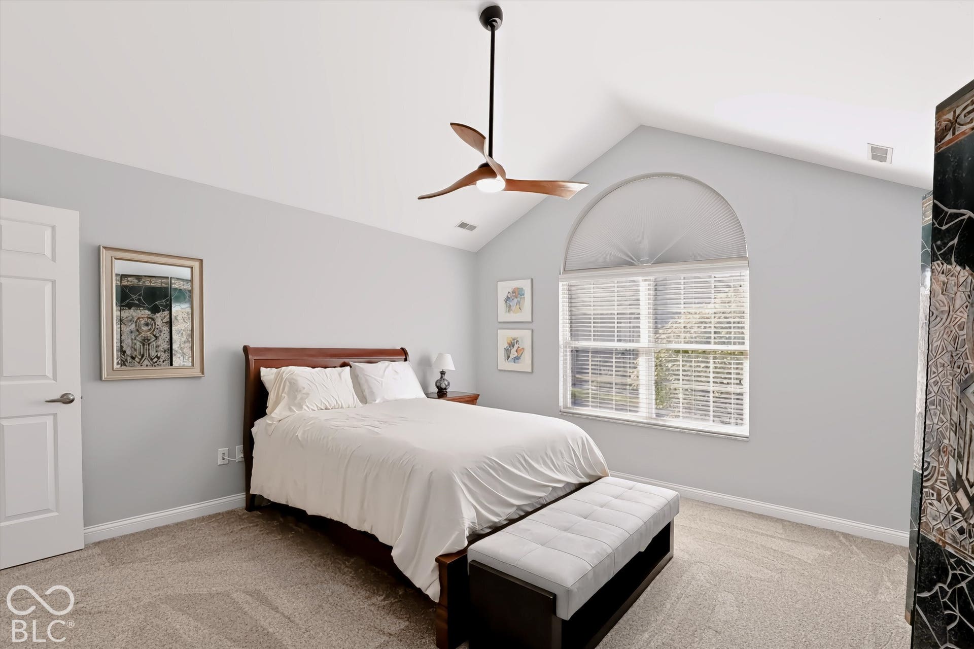Vaulted ceiling, arched window, ceiling fan, neutral carpet flooring, and a solid core door