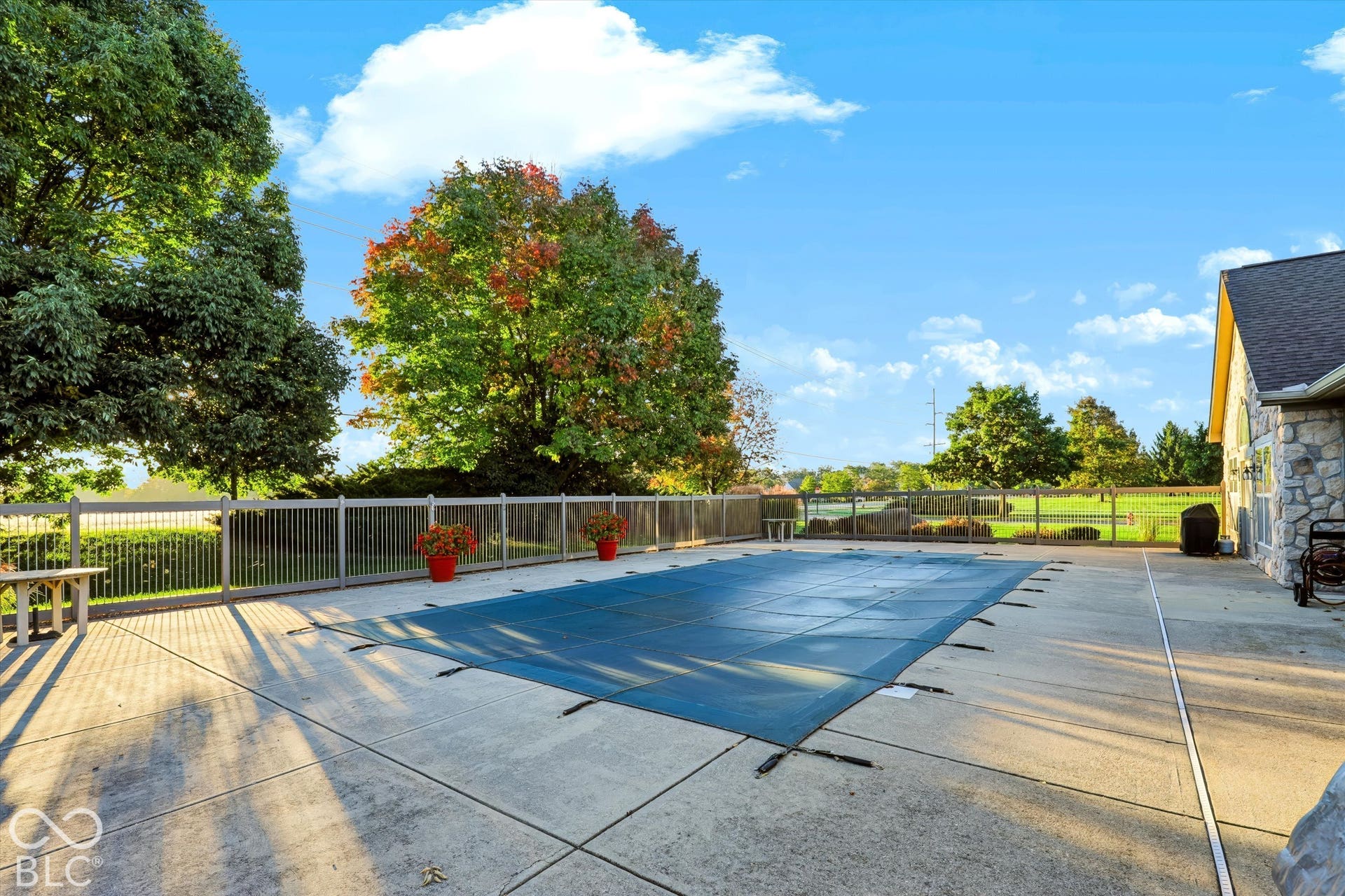 Fenced outdoor pool with concrete surround and mature perimeter trees