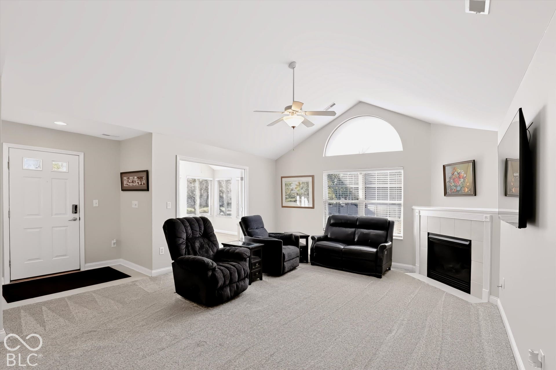 Vaulted ceiling with an arched transom window, a ceiling fan, and a fireplace with a white mantel