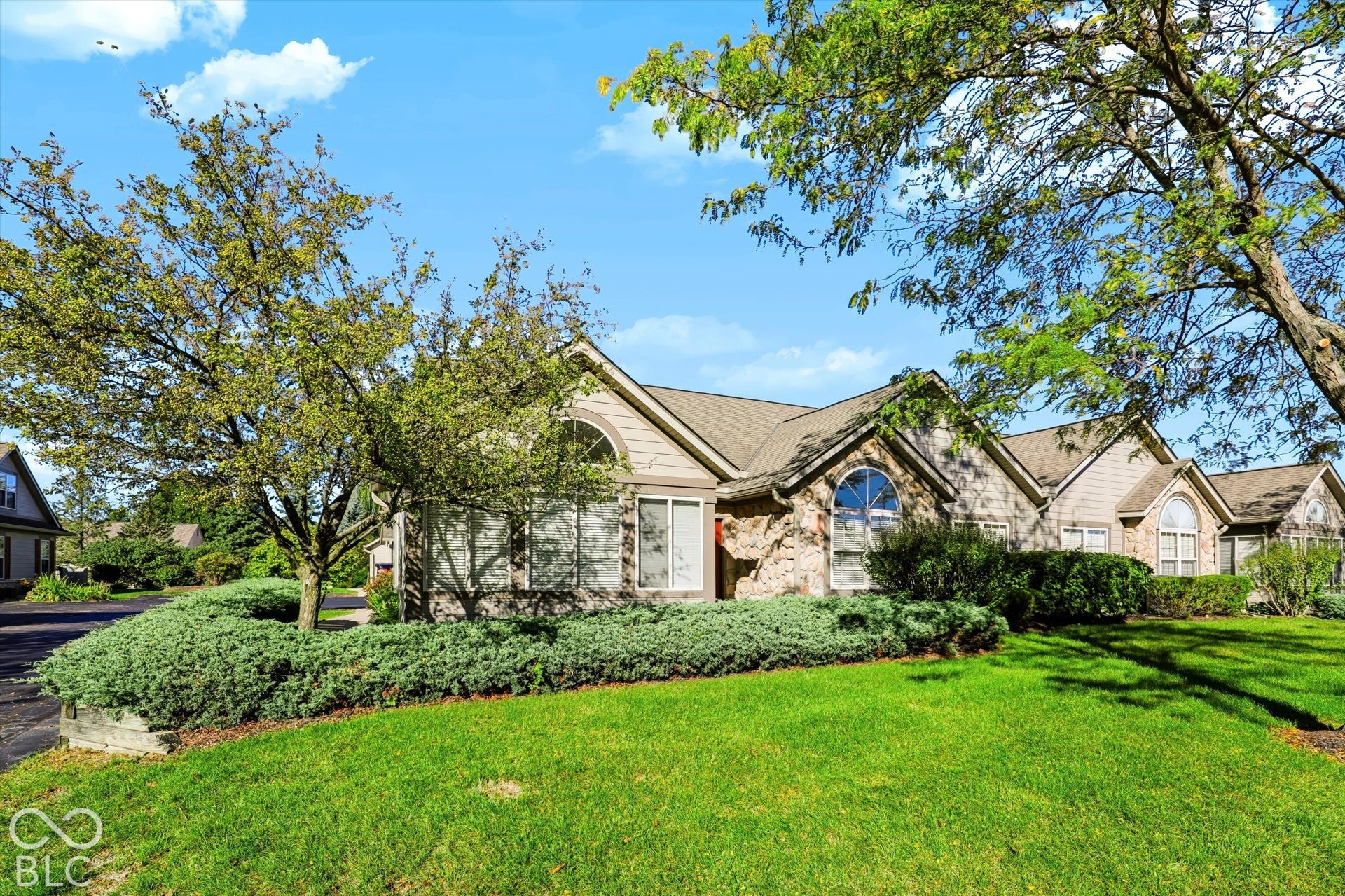 Stone and siding exterior with arched windows, gabled rooflines, and mature landscaping