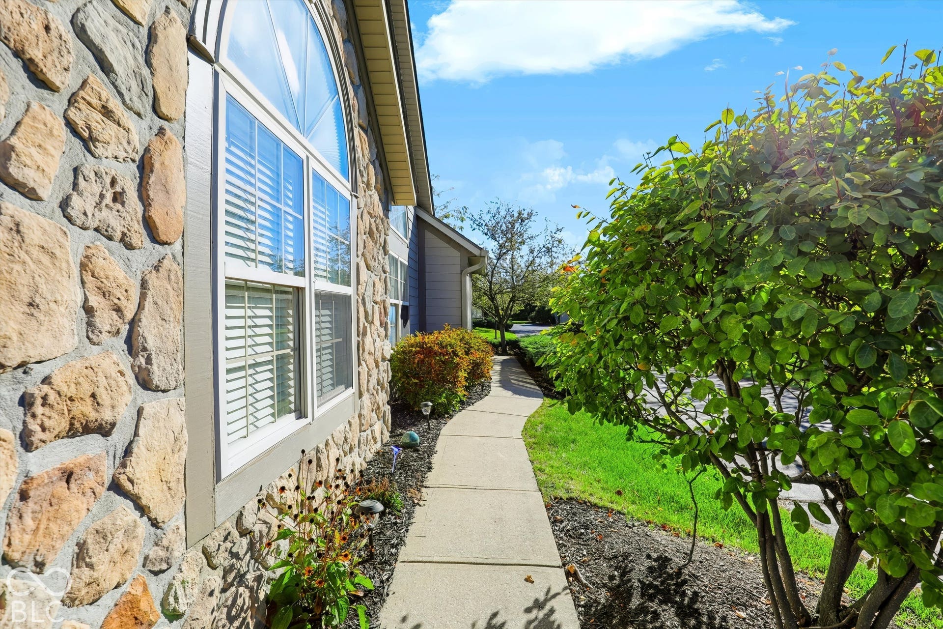 Stone veneer exterior with arched window, concrete pathway, and landscaped bed