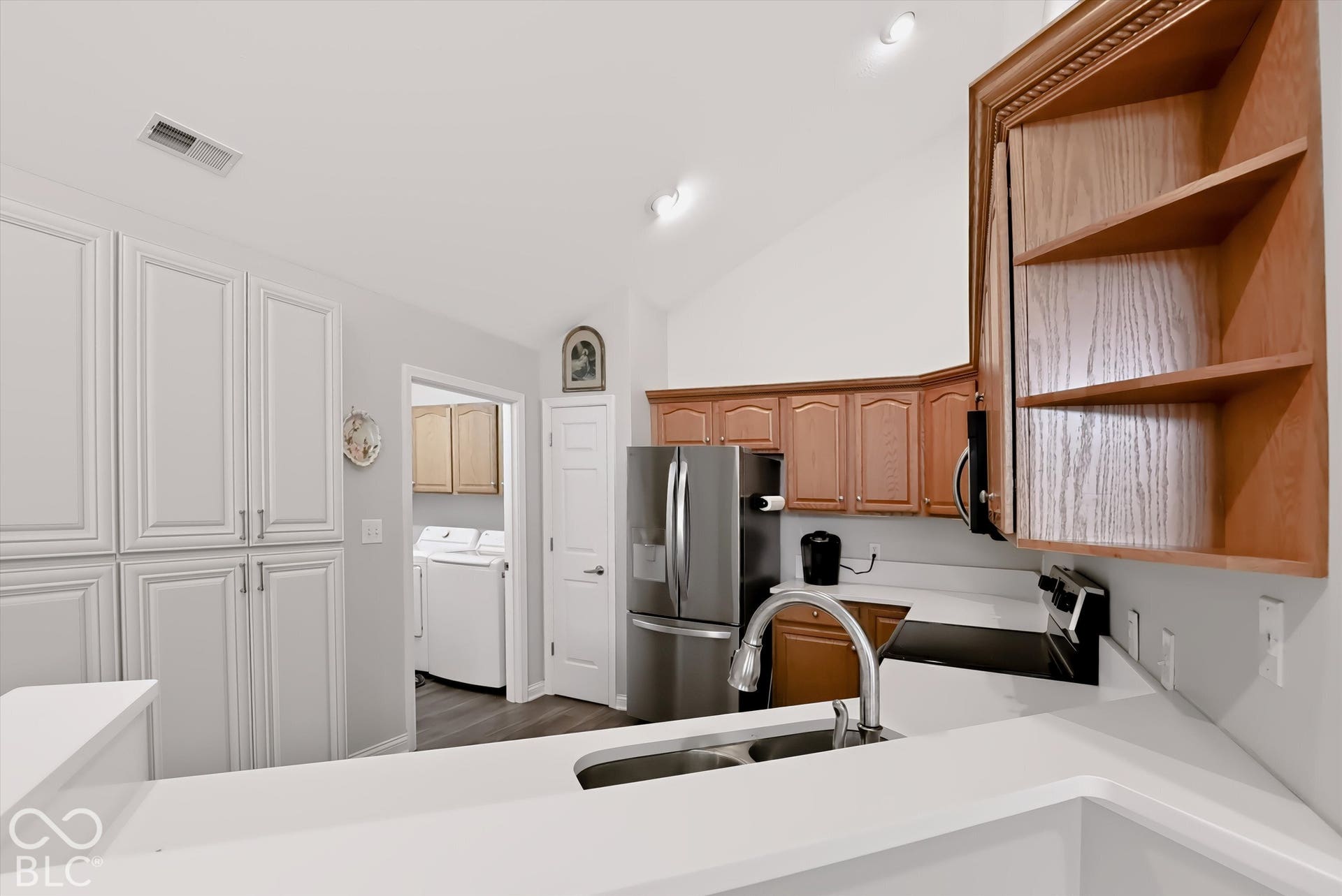 Kitchen featuring white cabinetry with silver-tone hardware, wood-finish upper cabinetry with interior shelving, stainless steel appliances, and a double basin sink