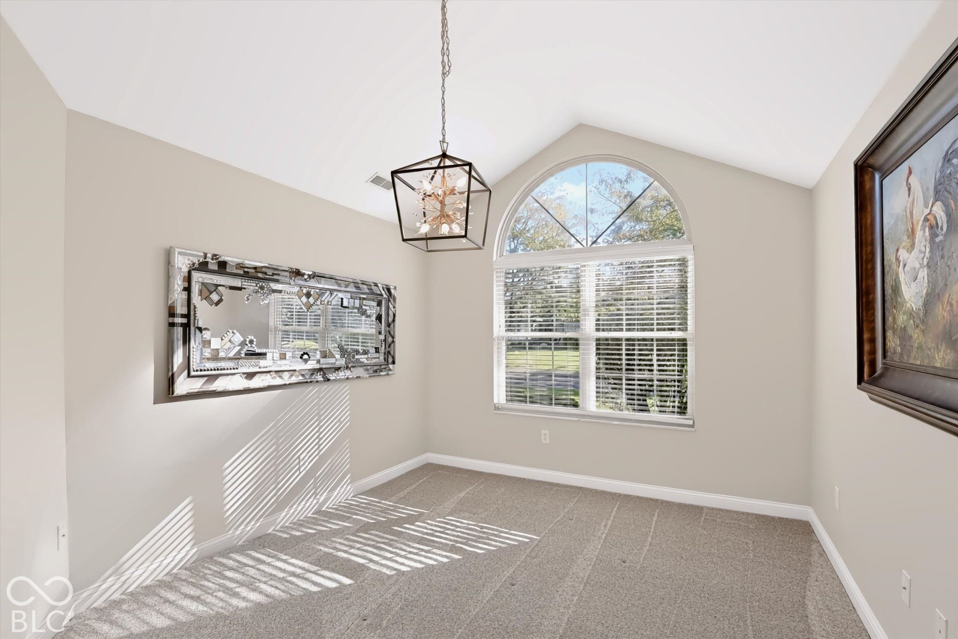 Vaulted ceiling with an arched window, suspended geometric light fixture, and neutral carpeting
