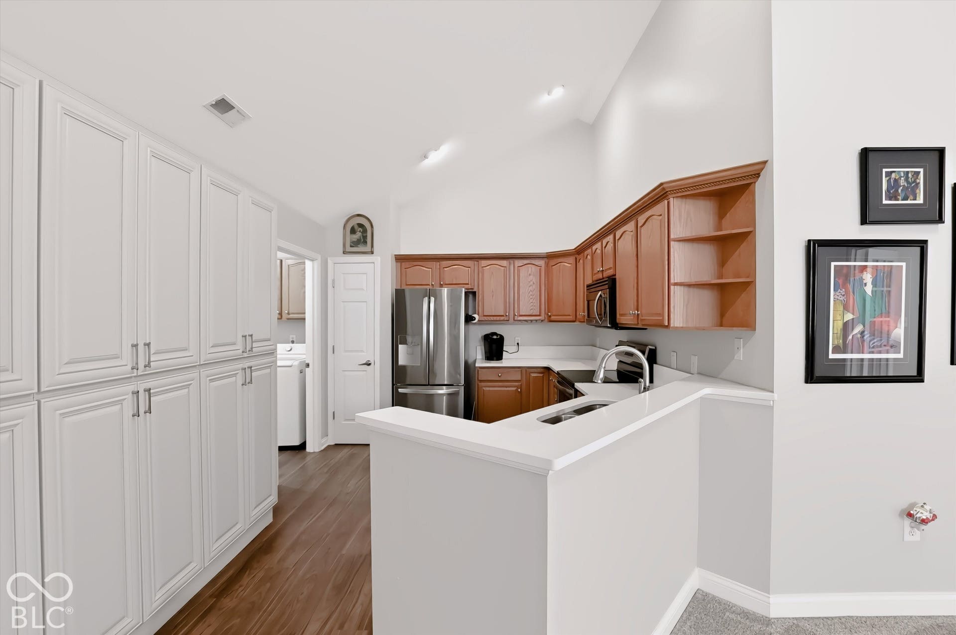 Vaulted ceiling kitchen featuring a stainless steel refrigerator, dark wood finish cabinetry, light countertops, and a built-in microwave
