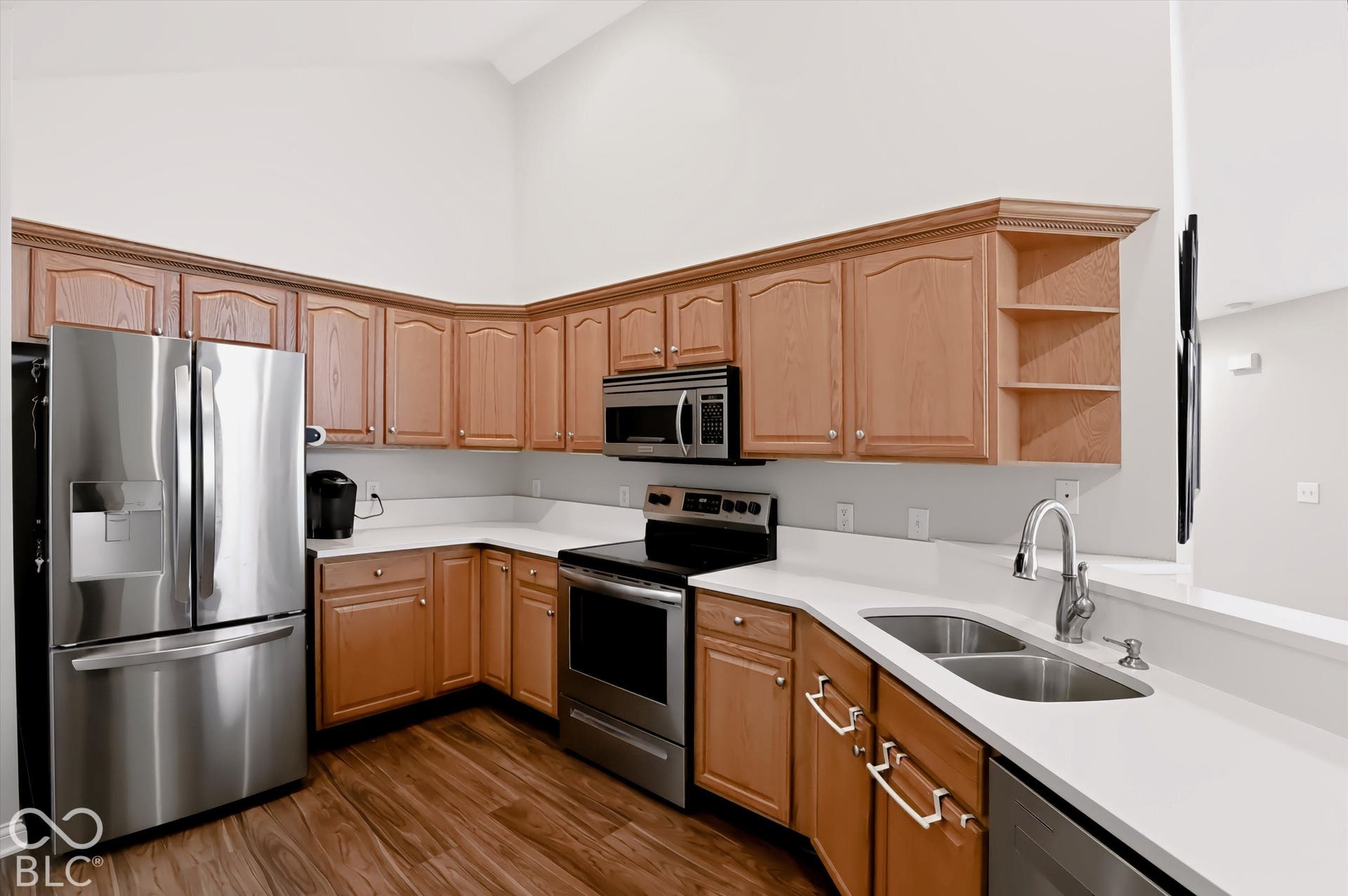 Kitchen featuring stainless steel appliances, wood-finish flooring, white countertops, a double basin sink, and wood cabinetry