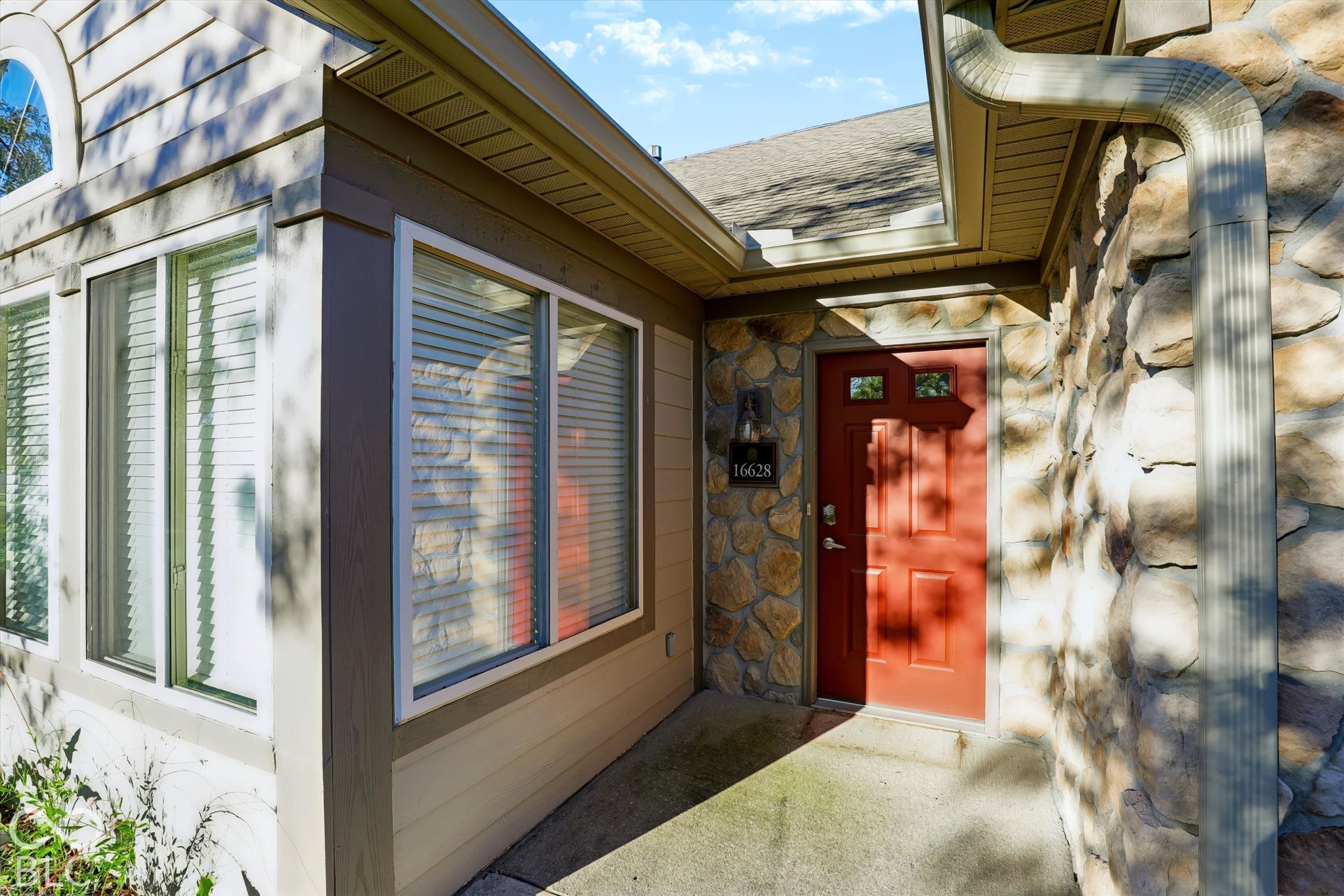 Entry with a paneled red door, stone facade, and horizontal siding