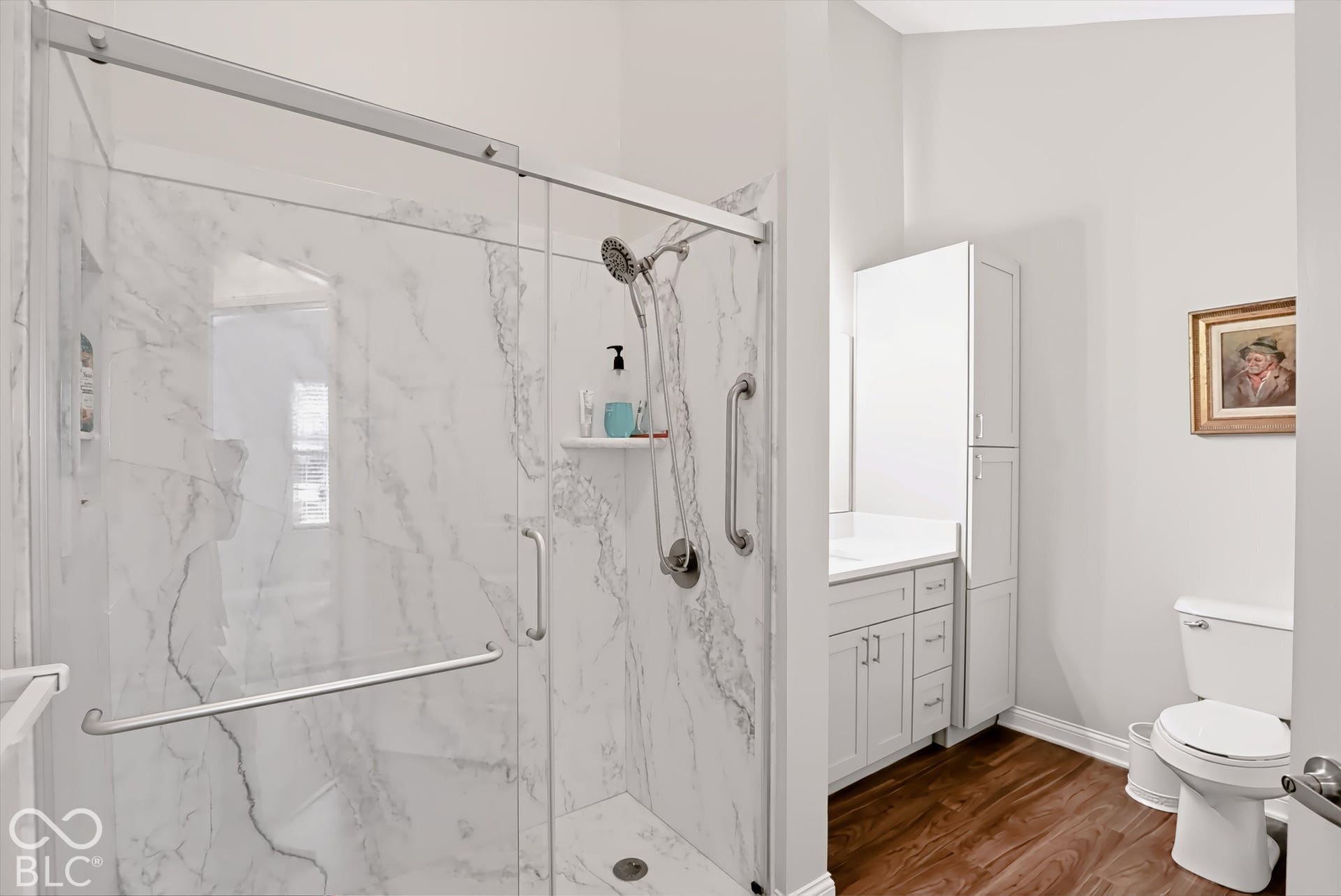 Glass-enclosed shower with white marble-finish wall tile, a built-in shower shelf, and grab bars