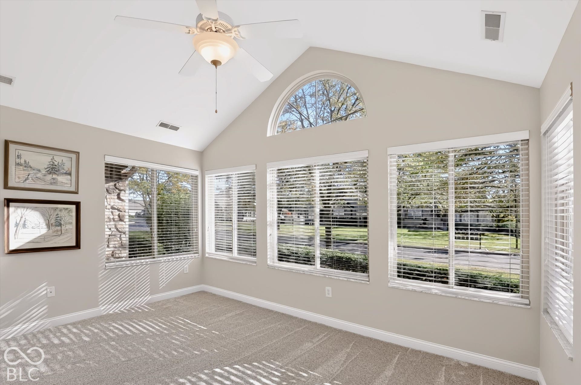 Vaulted ceiling with a ceiling fan, arched transom window, multiple large windows with blinds, and neutral carpeting