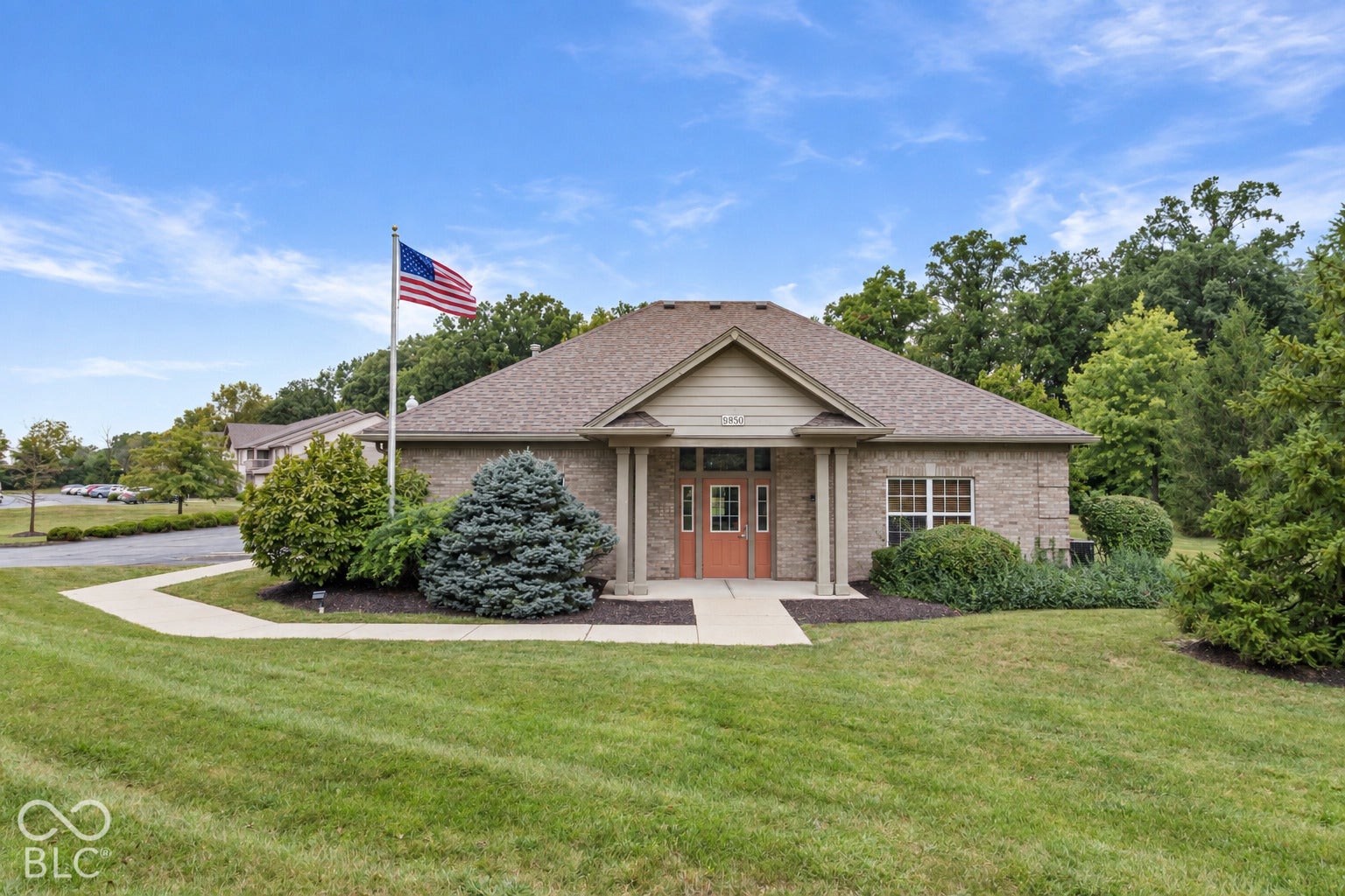 Charming brick residence featuring a covered front portico with classical columns, manicured landscaping with mature evergreen shrubs, expansive lawn, and a curved driveway
