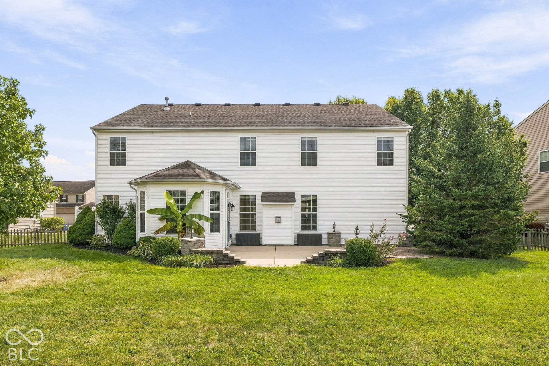 Rear exterior featuring white siding, a bay window with a dark roof, and a ground-level patio