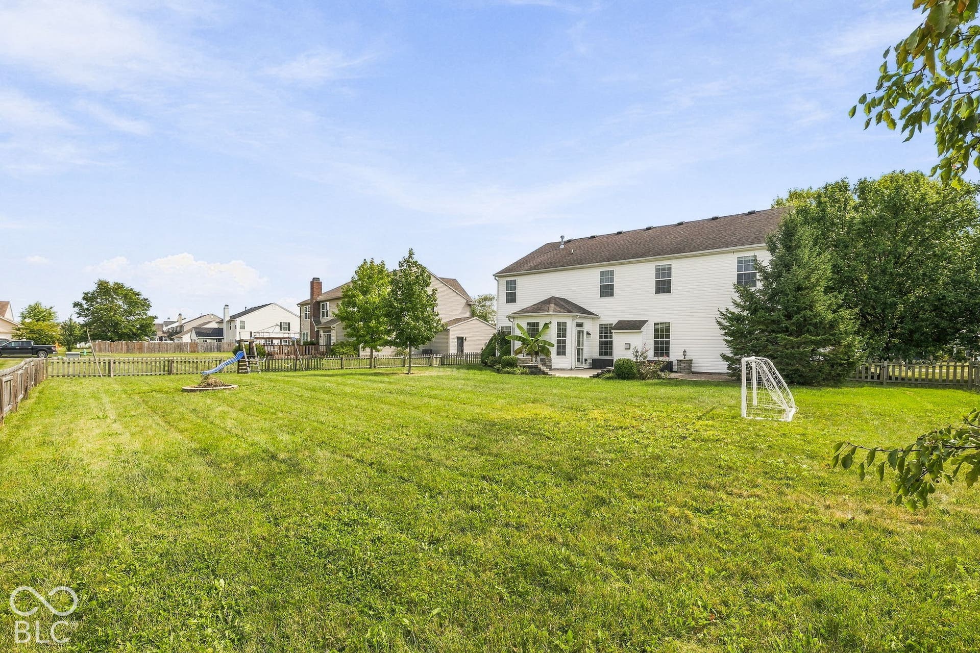 Expansive backyard featuring a large green lawn, perimeter wood fencing, and a white siding exterior with multiple windows