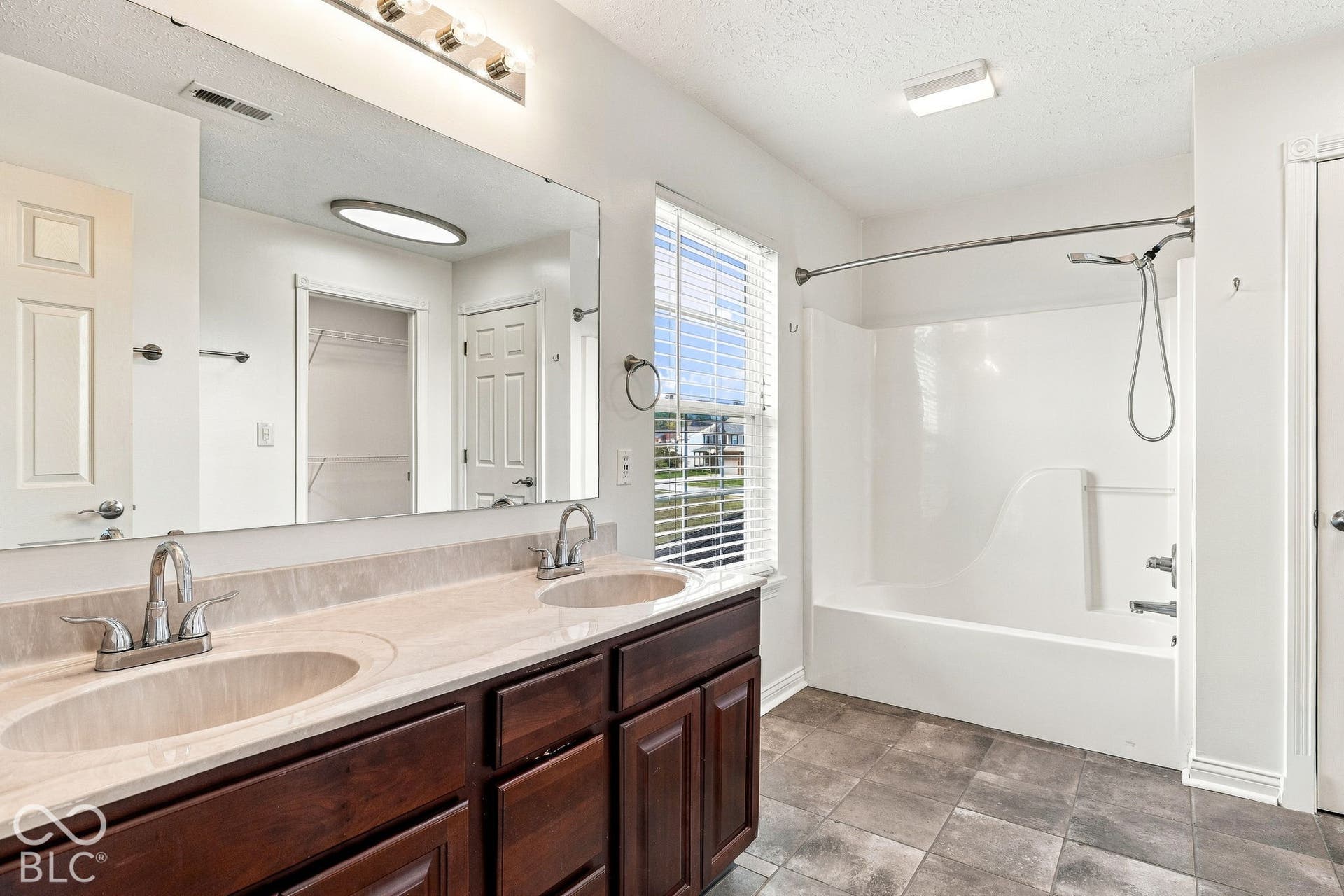 Dual basin vanity with a light-toned countertop, wood-finish cabinetry, and a full-width mirror