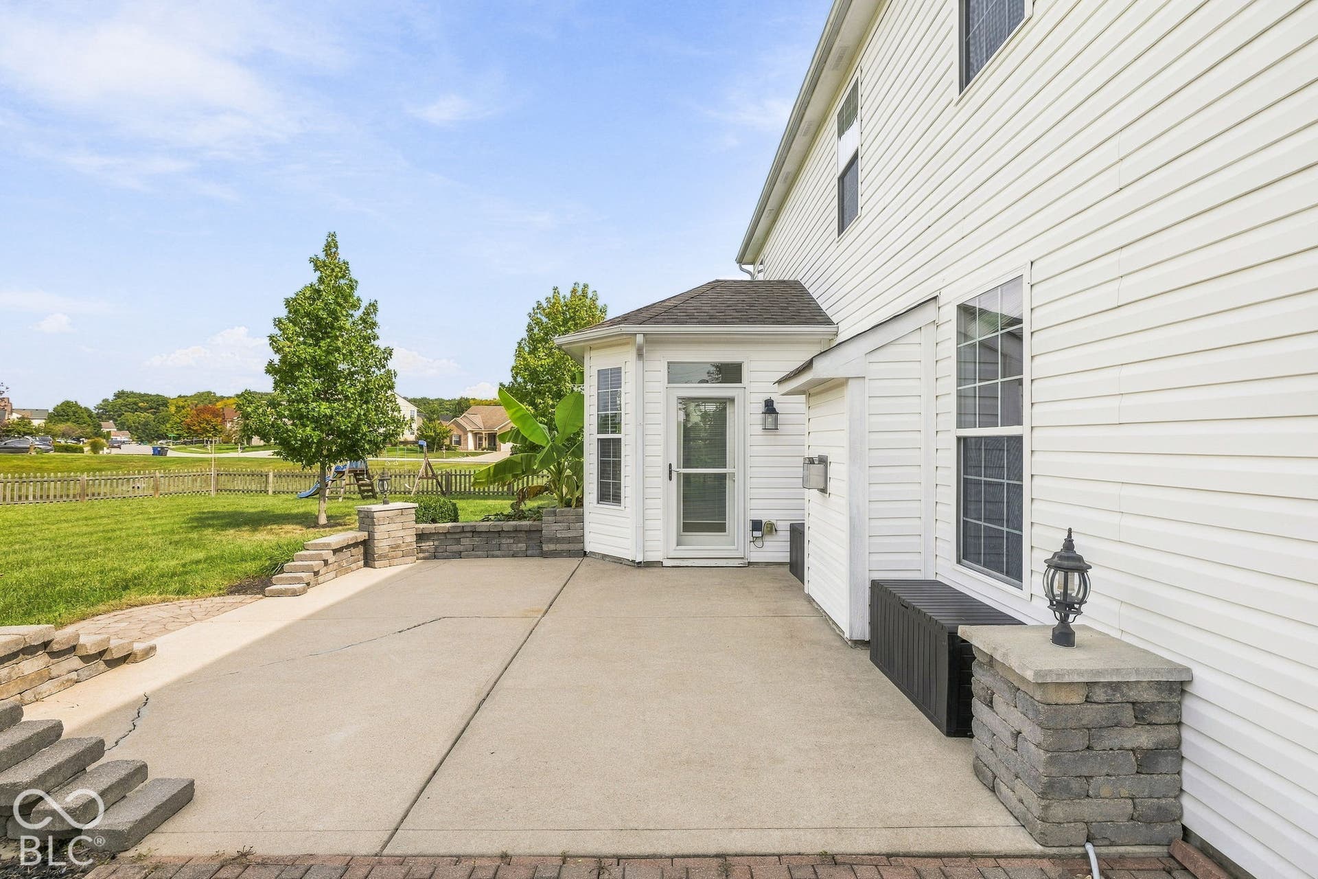 Expansive concrete patio with block retaining walls, white vinyl siding, and a sunroom with direct access