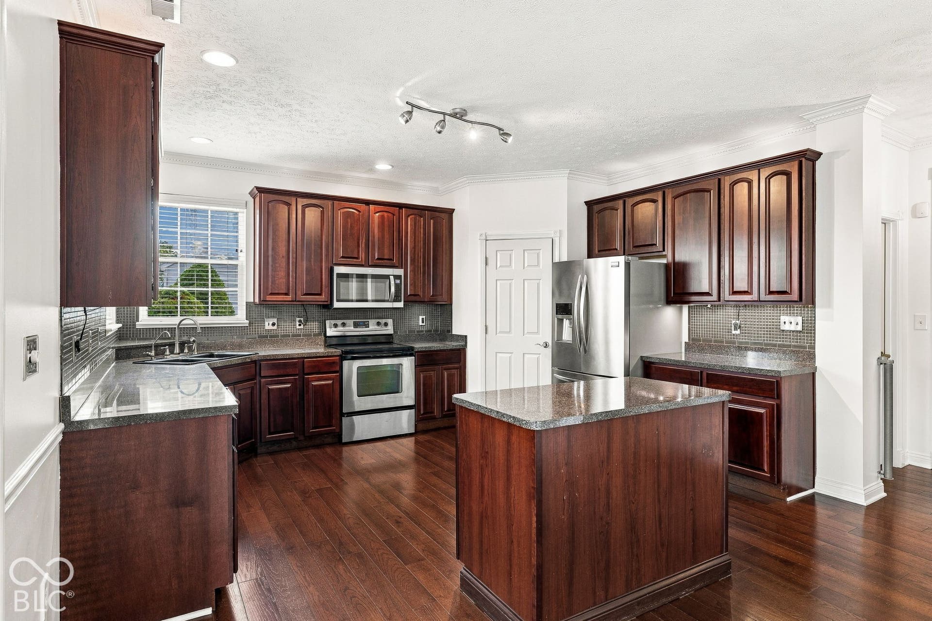 Kitchen featuring wood-finish flooring, dark wood cabinetry, granite countertops, and stainless steel appliances