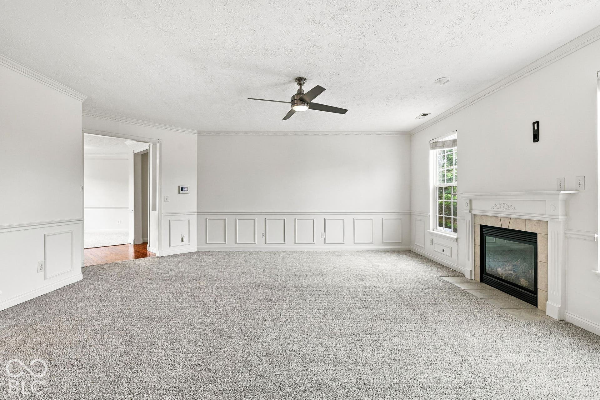 Living space featuring a built-in fireplace with a decorative mantel, multiple windows, wainscoting, and a ceiling fan