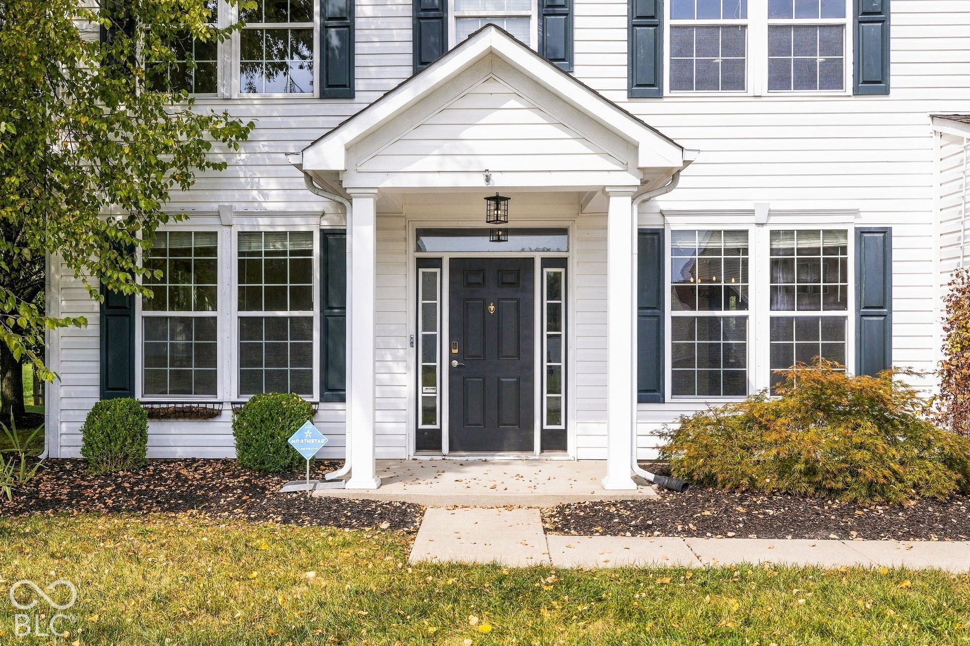 White siding exterior with a dark-paneled front door, accented by white pillars and dark window shutters