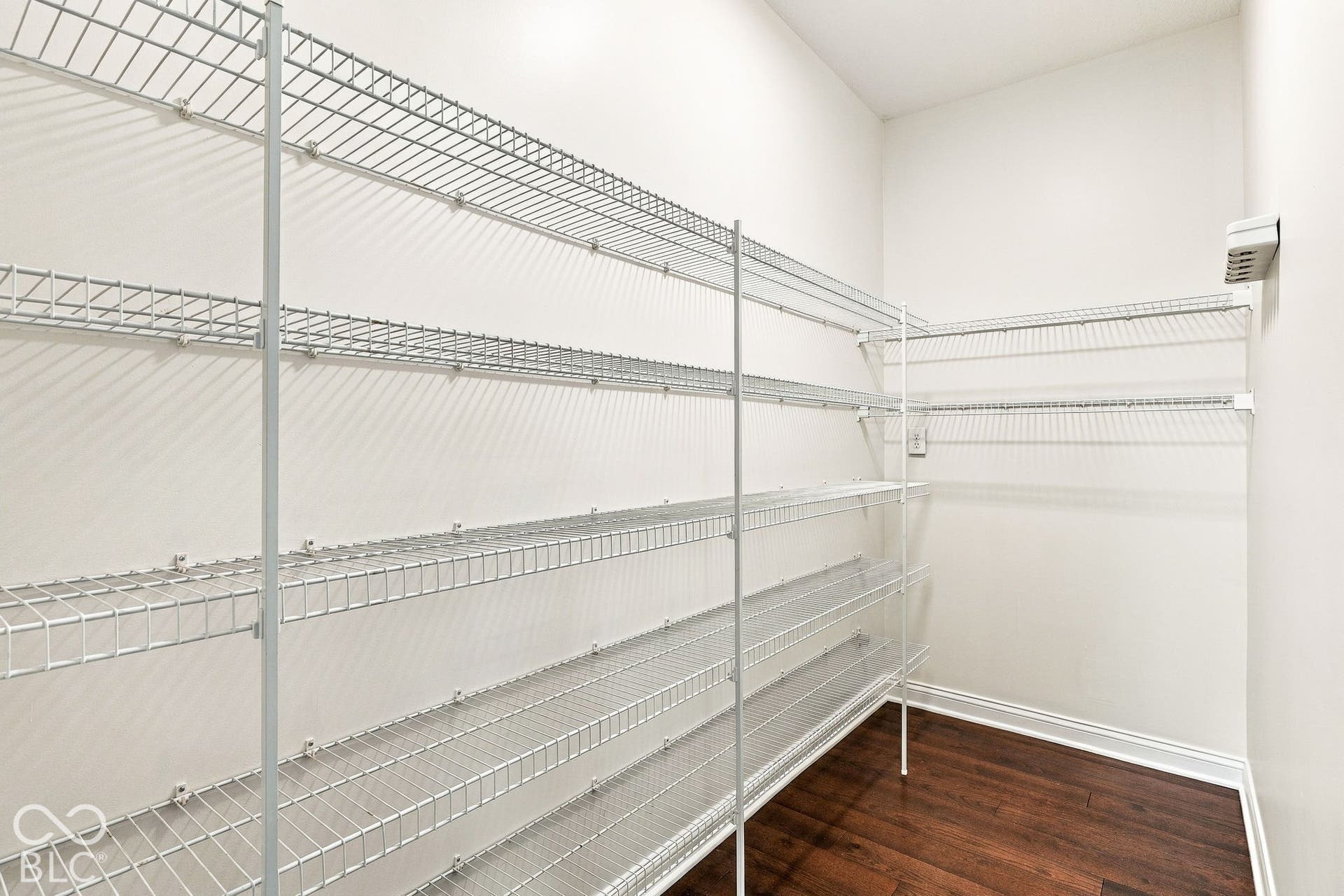 Walk-in closet with extensive wire shelving, white walls, dark wood-finish flooring, and white trim