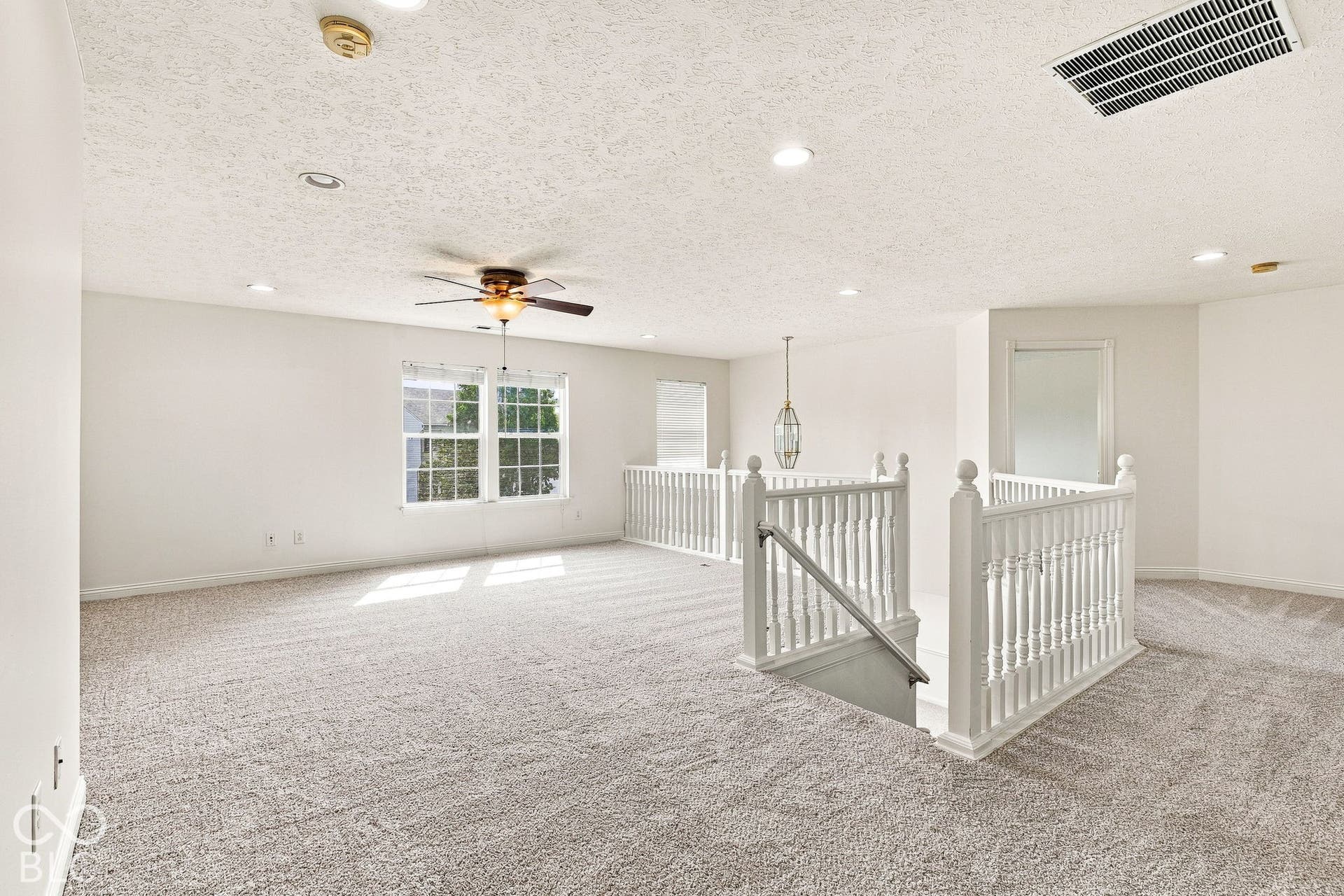 Expansive carpeted loft area with recessed lighting, ceiling fan, and white spindle railing