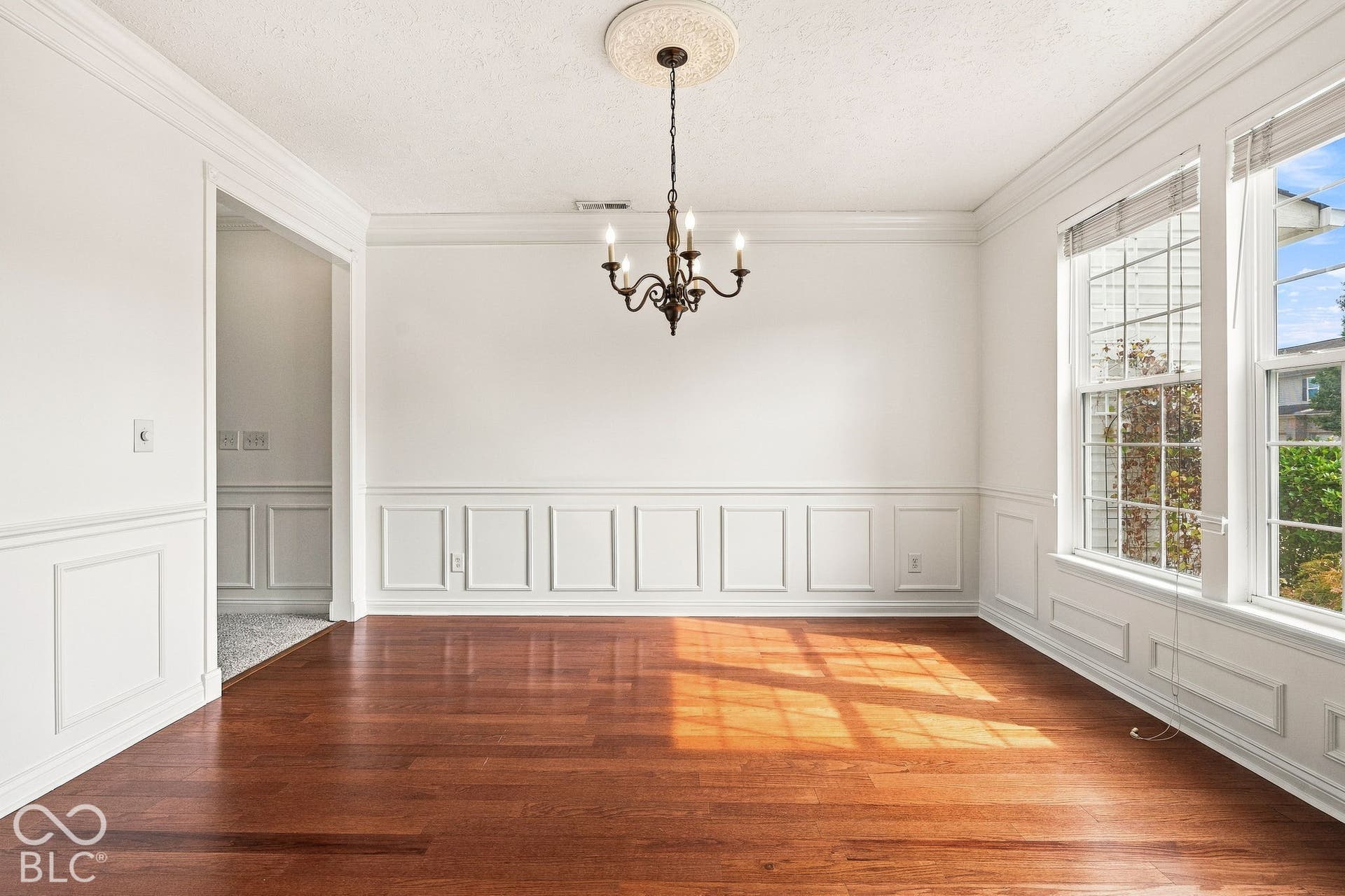 Hardwood-finish flooring, wainscoting, crown molding, double windows, and a chandelier with a ceiling medallion