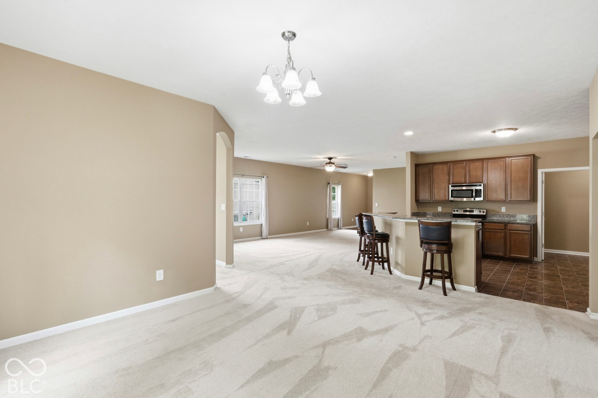 Spacious open-concept living area featuring a kitchen island with seating, stainless steel appliances, wood cabinetry, and a ceiling fan