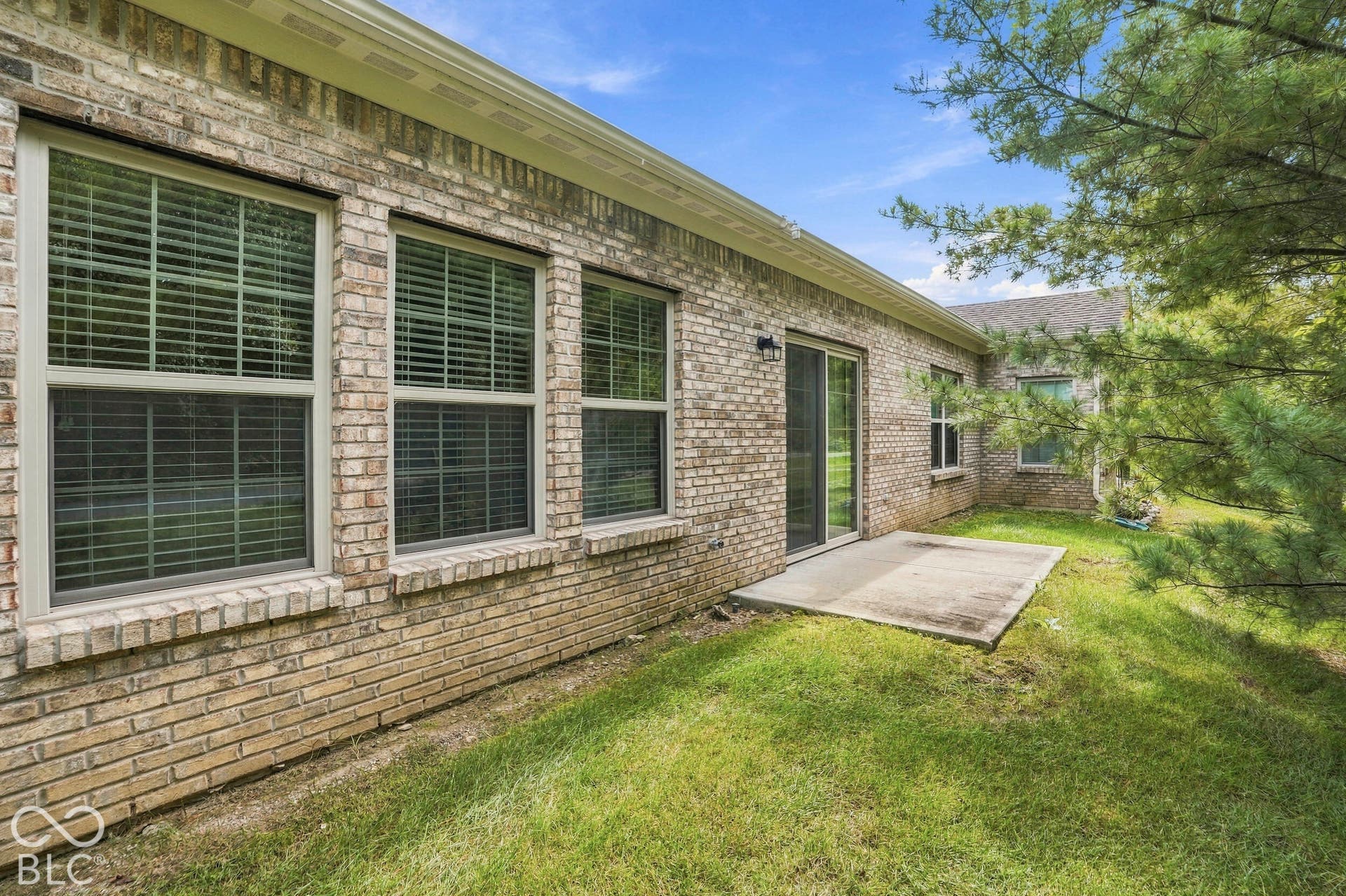 Brick exterior featuring multiple windows with blinds, a sliding glass door, and a concrete patio